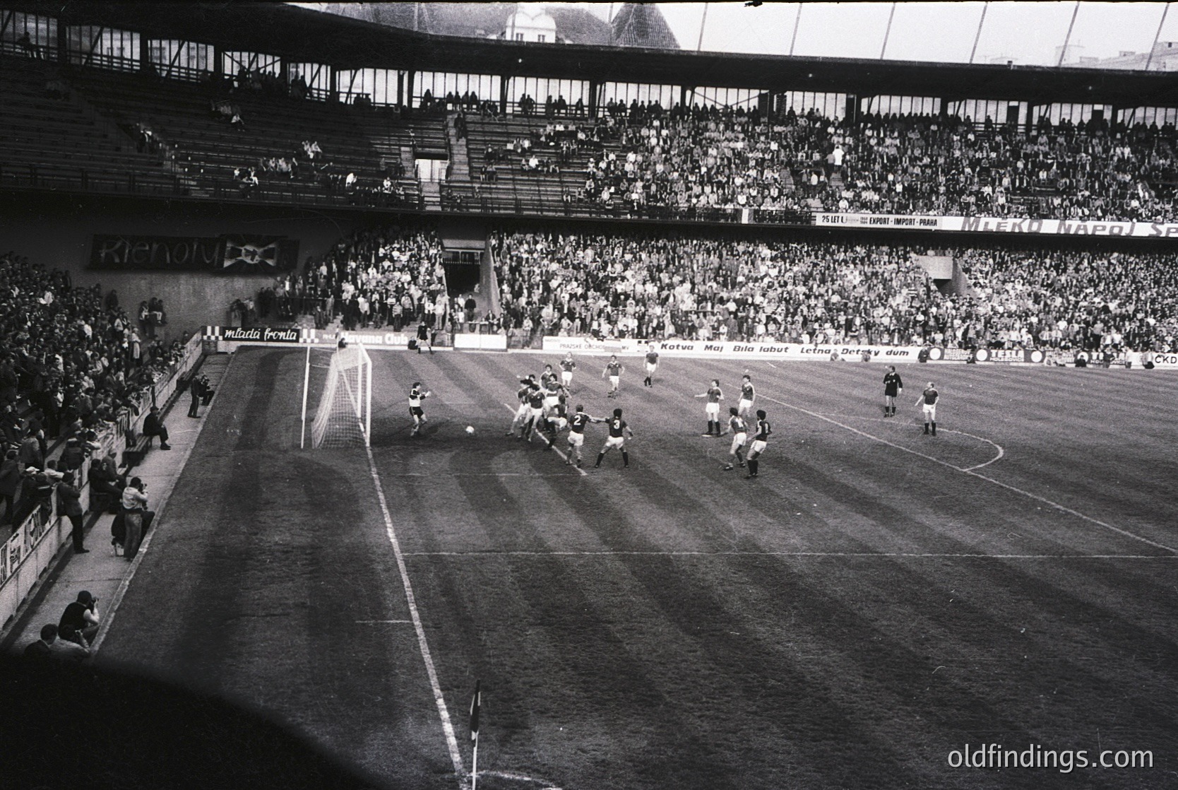 Black-and-white shot of a packed stadium during a high-stakes soccer match, likely 1960s–1970s. Crowds fill tiered stands, while players clash near the goal. Visible signage includes "Mundo Deportivo" and "Barcelona." Classic retro sports aesthetic.
