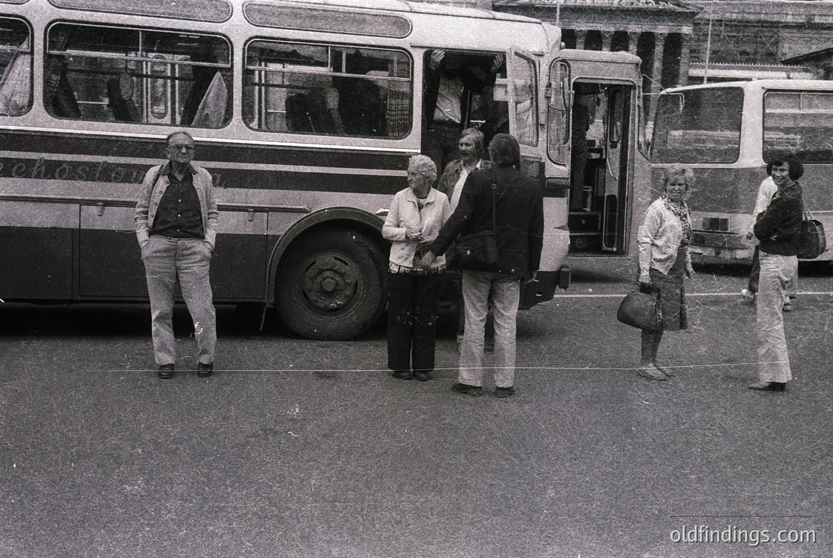 Vintage black-and-white street scene featuring a group of people boarding a mid-20th-century double-decker bus. Urban setting with visible bus stop signage ("Bus Stop") and classic bus design. Men in suits, women in dresses and skirts; one man in a backpack. Likely 1960s–1970s European city.