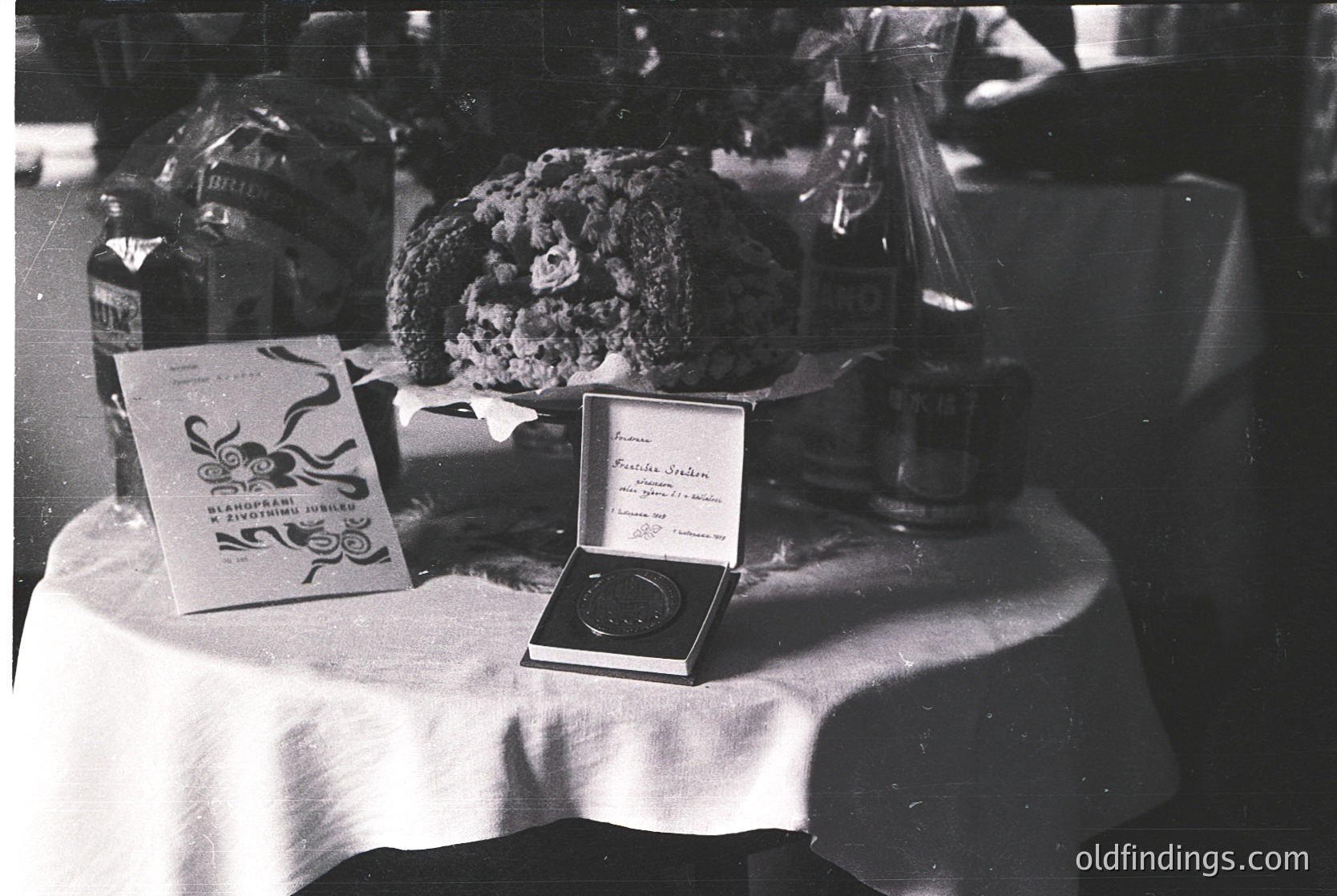 Vintage black-and-white table display featuring a **1960s-era** award box, likely a **gold medal**, inscribed *"Prix de la Ville de Paris"* with a 1963 date. Surrounding items include a **cake or pastry** in a decorative stand, a **canned beverage** (likely a soft drink), and a **packaged food box** with Cyrillic script. Tablecloth and lighting suggest an indoor event, possibly a **culinary or gastronomic competition**.