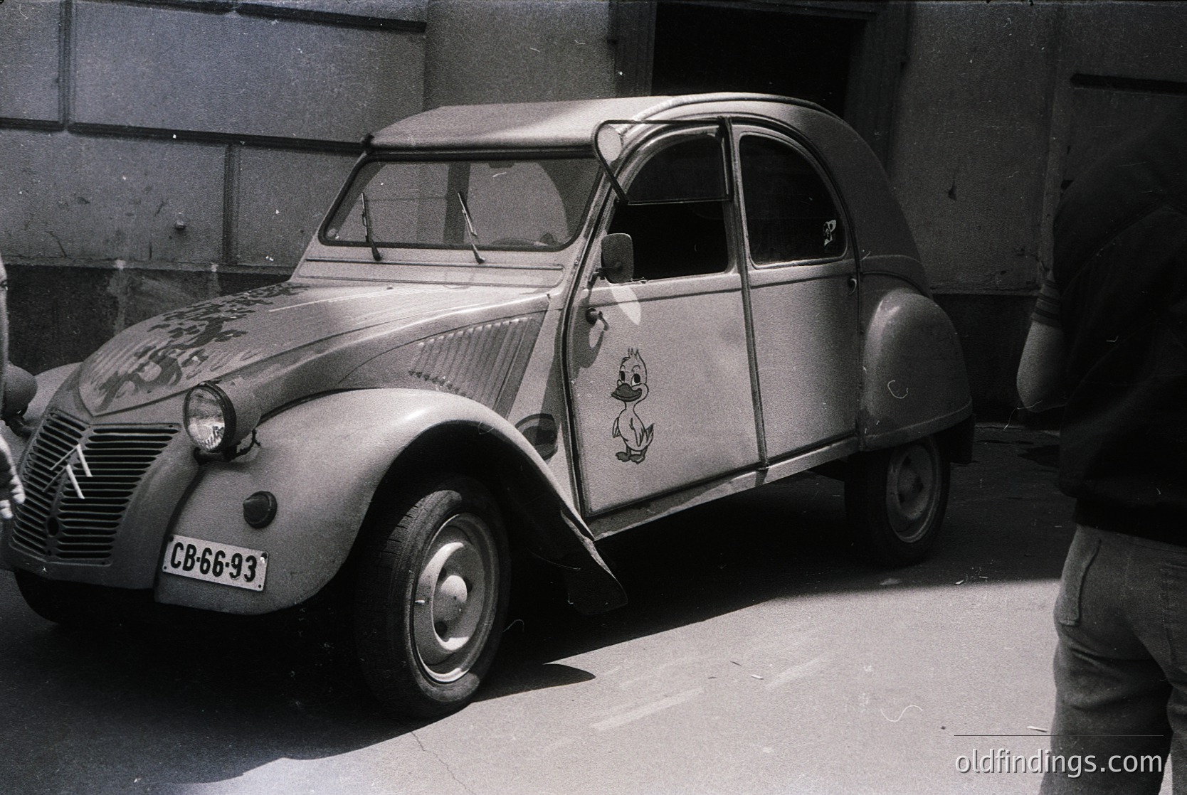 Classic Citroën 2CV with vintage French maritime decals, parked beside a concrete wall. Distinctive rounded body, small wheels, and CB-66-93 license plate suggest mid-20th century (1950s–1960s). Ideal for automotive history, retro design, or European travel archives.