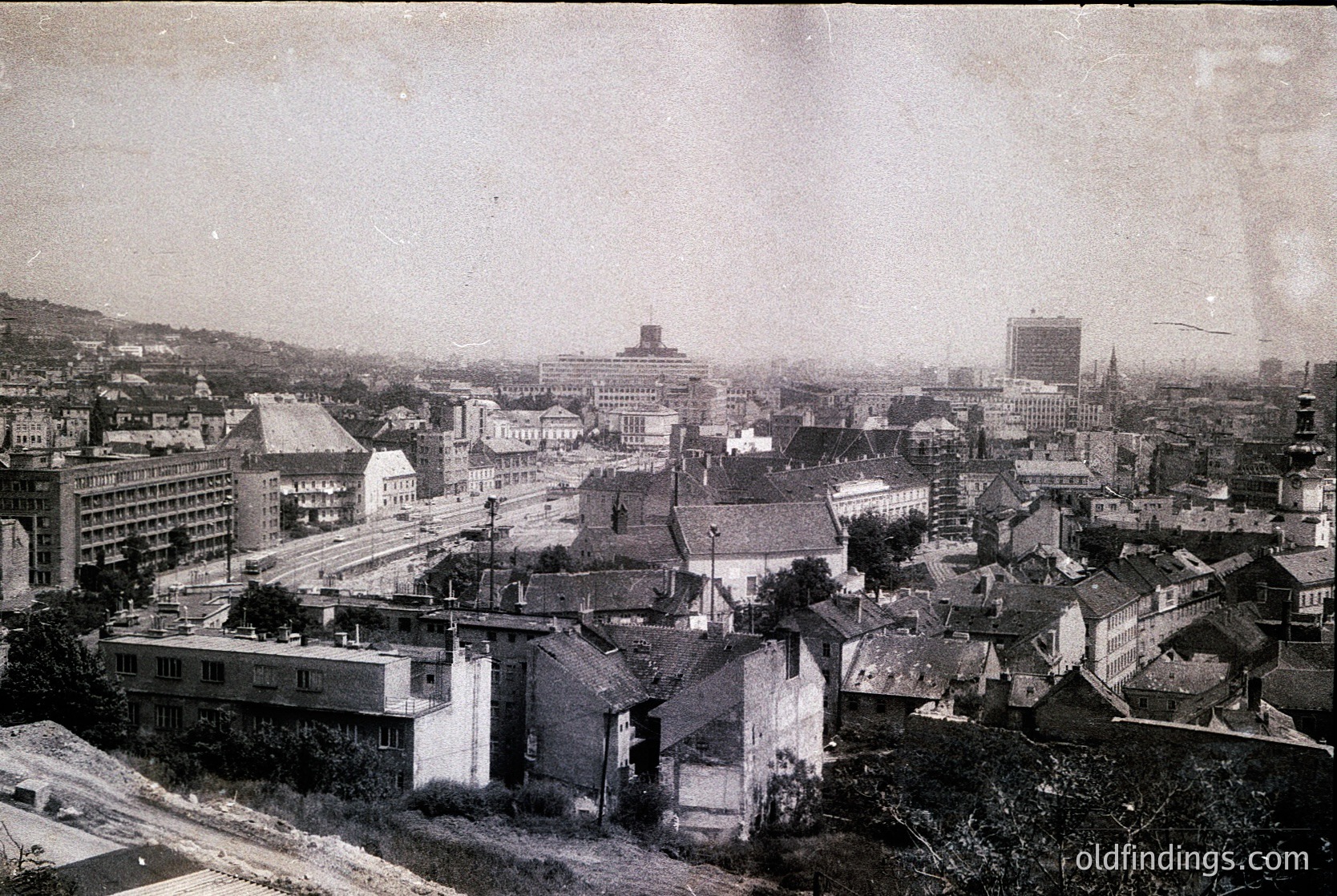 Early 20th-century urban panorama featuring dense, low-rise buildings with flat roofs and minimalist architecture. Prominent railway tracks and elevated train line dominate the center, suggesting industrial transport hub. Skyline includes a mix of brick and concrete structures, with a few taller buildings hinting at early modernization. Likely Eastern European cityscape, possibly or , circa –.