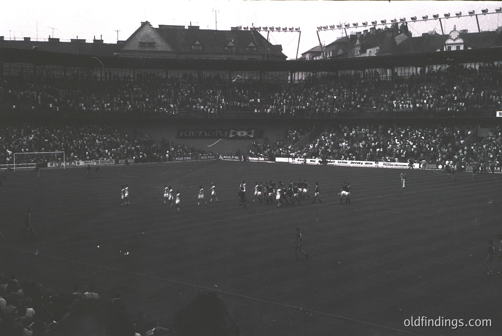 Black-and-white stadium shot showing a packed 1950s-era football match with tiered seating and flag-lined rooftops. Players and spectators fill the field and stands, indicating high attendance. Advertising banners and "Austria" signage visible.