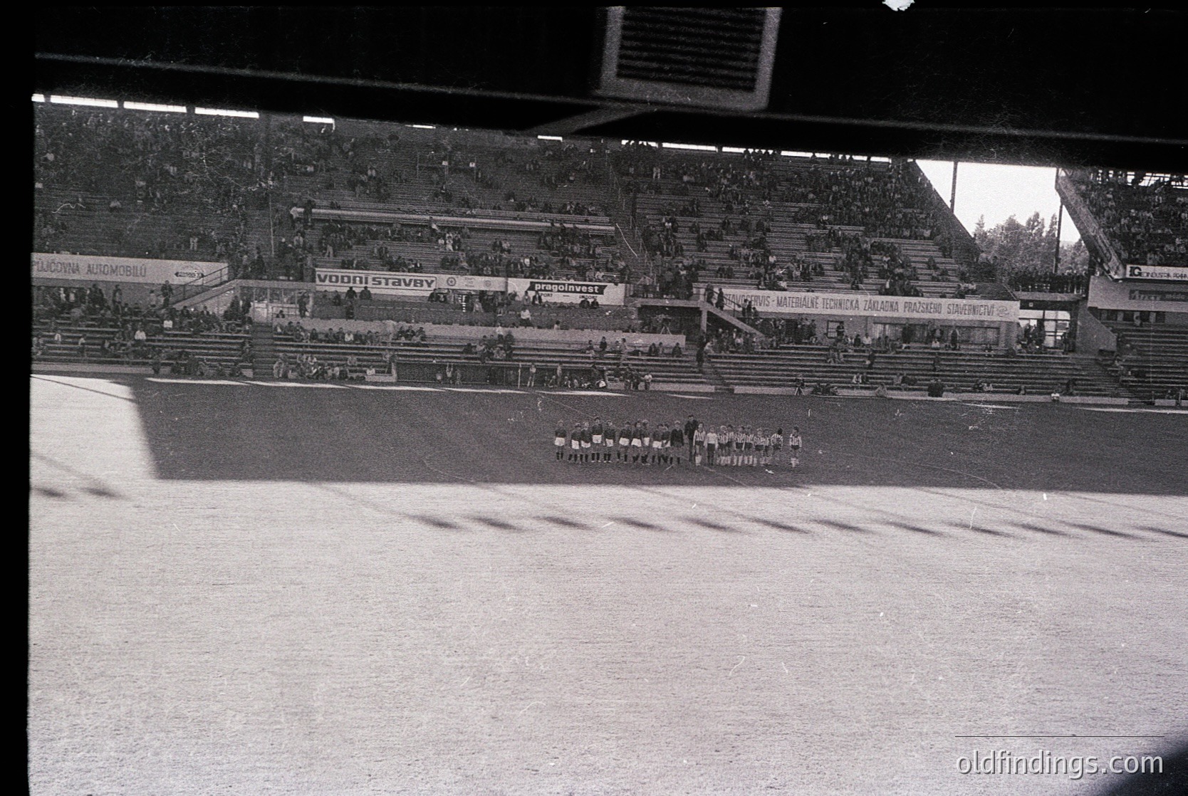 Vintage black-and-white stadium shot showing a large, tiered seating area with sparse crowds. Prominent banners in Cyrillic script suggest Eastern European location, likely Bulgaria. Central field features a marching band or formation in disciplined rows. Architectural details include concrete stands and floodlight towers. Circa 1960s–1980s.