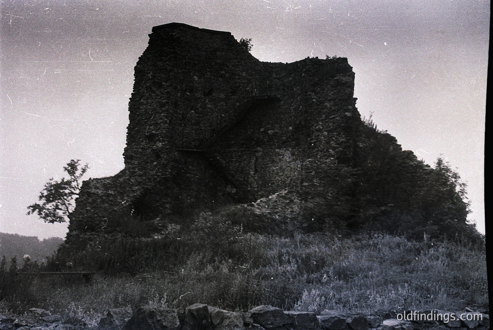 Ruined medieval stone fortress perched on rocky hillside, surrounded by sparse vegetation. High-angle vintage photograph captures weathered walls and crumbling towers. Likely Eastern European, 19th–early 20th century.