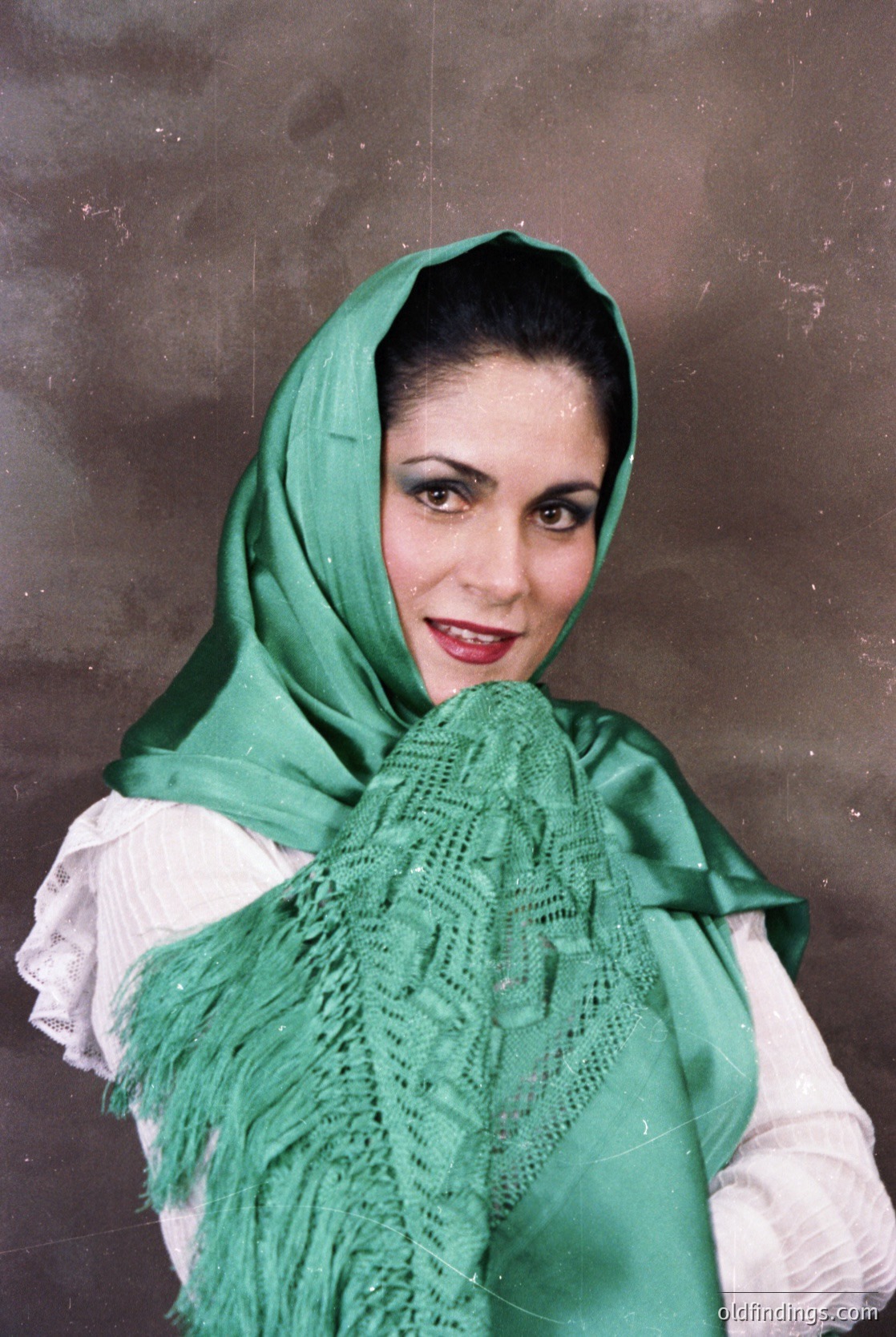 Portrait of a woman in traditional Middle Eastern attire, featuring a green lace headscarf and draped shawl over a white blouse. The intricate lacework suggests cultural or regional significance. Likely 20th-century studio portrait.