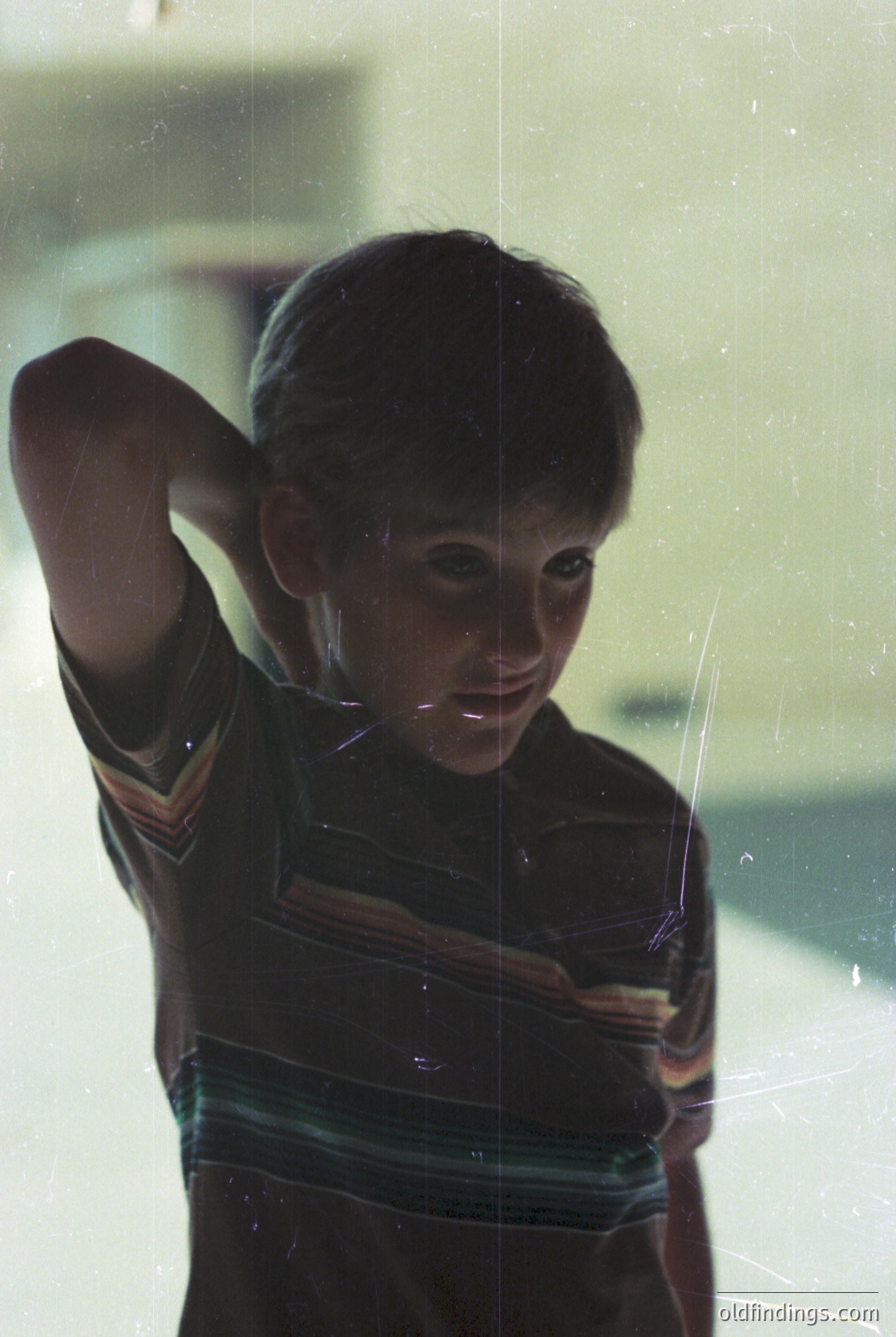 Vintage portrait of a young boy in a striped sweater, captured through a window with spiderweb reflections. Mid-20th century style, likely 1950s-1960s. Candid expression and lighting suggest a candid, documentary-style shot.
