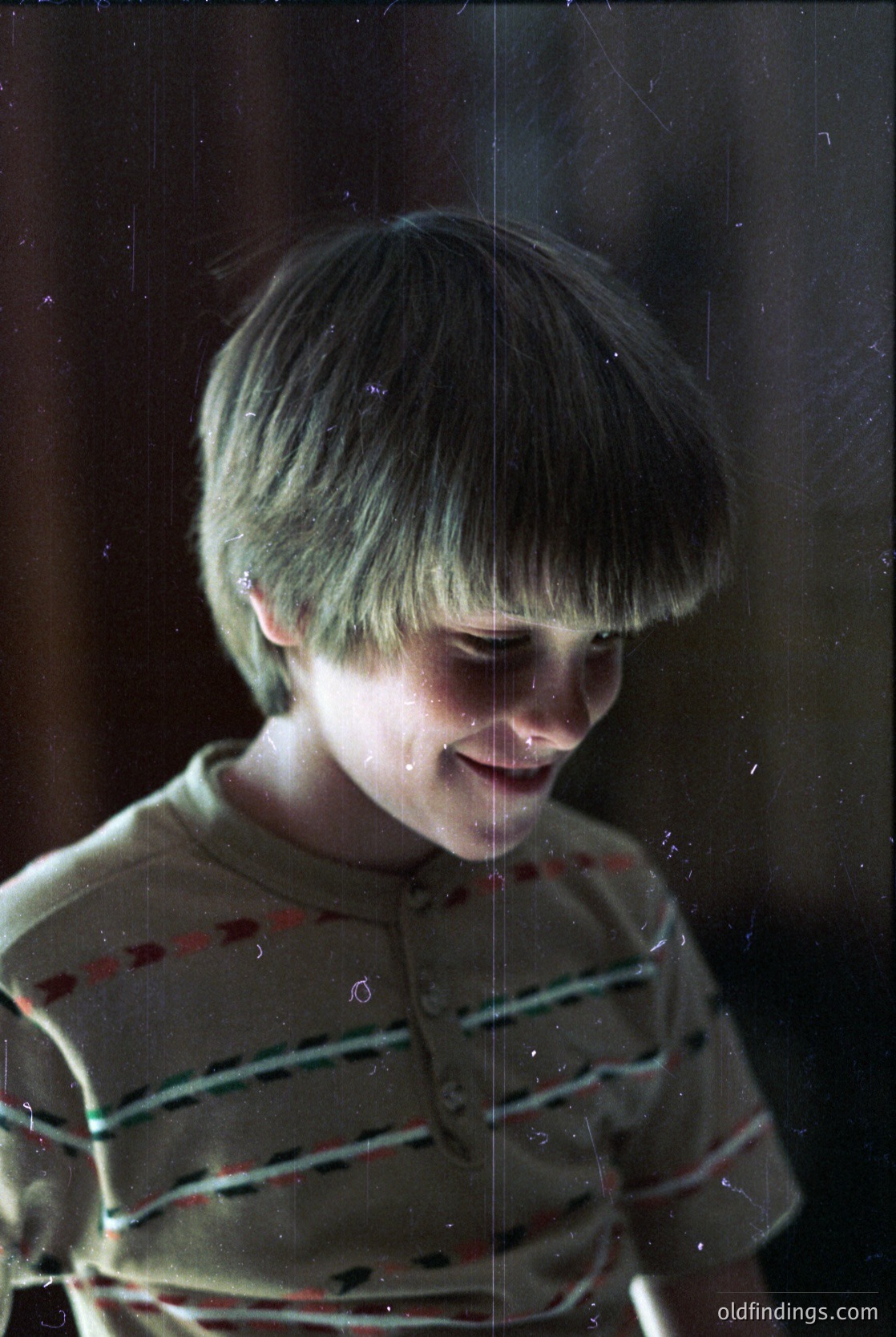 Vintage black-and-white portrait of a smiling child with short, neatly parted bangs, wearing a striped sweater. Raindrops blur the window behind, suggesting an indoor moment during wet weather. Likely mid-20th century (1950s–1970s) based on styling and film grain.