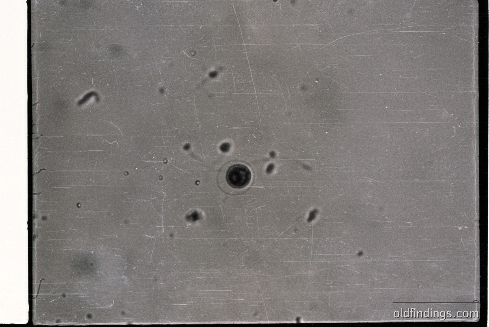 Vintage black-and-white close-up of a textured concrete surface with pockmarks and linear scratches, likely from industrial use or construction. The central hole suggests wear or damage.