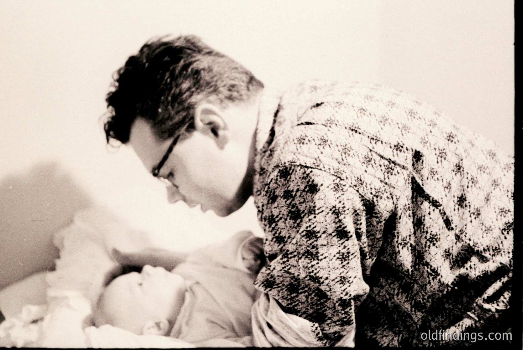 A man in a striped shirt tenderly cradles a newborn in a simple indoor setting, likely a hospital or home birth scene. The vintage sepia tone suggests or . The intimate moment captures paternal bonding.