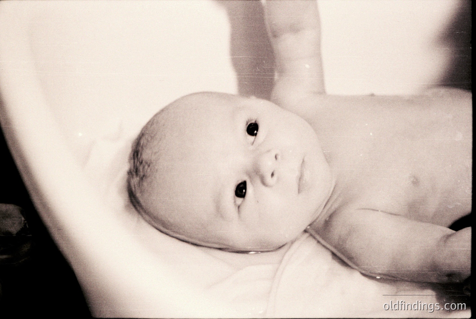 Black-and-white candid of an infant in a bathtub, likely mid-20th century. Soft focus highlights innocence; visible birthmarks and diaper suggest domestic setting. Vintage grain adds nostalgic texture.