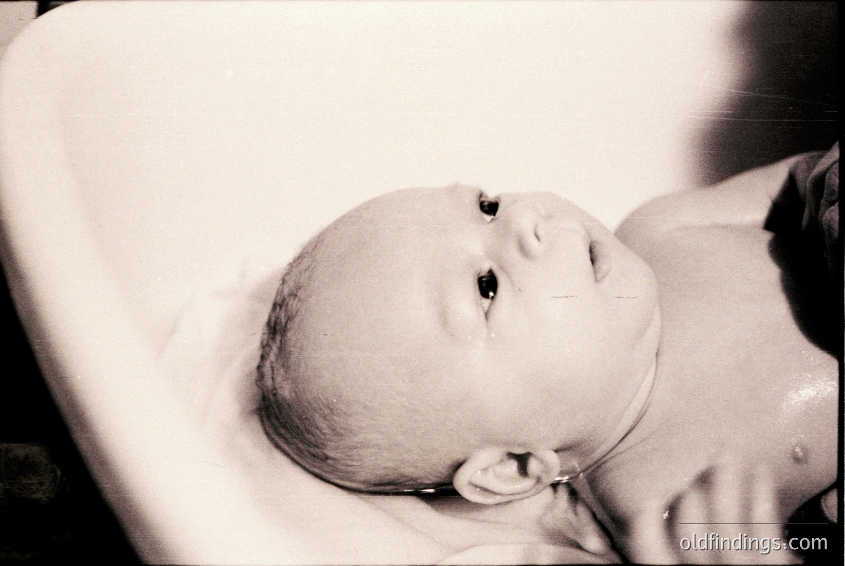 Black-and-white portrait of an infant in a swaddling cloth, likely mid-20th century. Soft focus highlights delicate features and serene expression. Classic vintage aesthetic ideal for historical or nostalgic content.