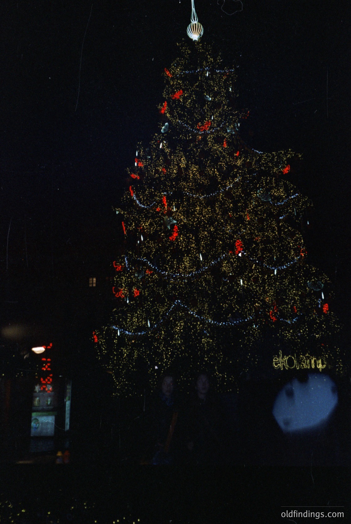 Vintage-style illuminated Christmas tree decoration with reflective gold foil, red accents, and "elOma" branding. Likely 1960s–1970s holiday marketing. Ideal for retro-themed design or festive stock imagery.