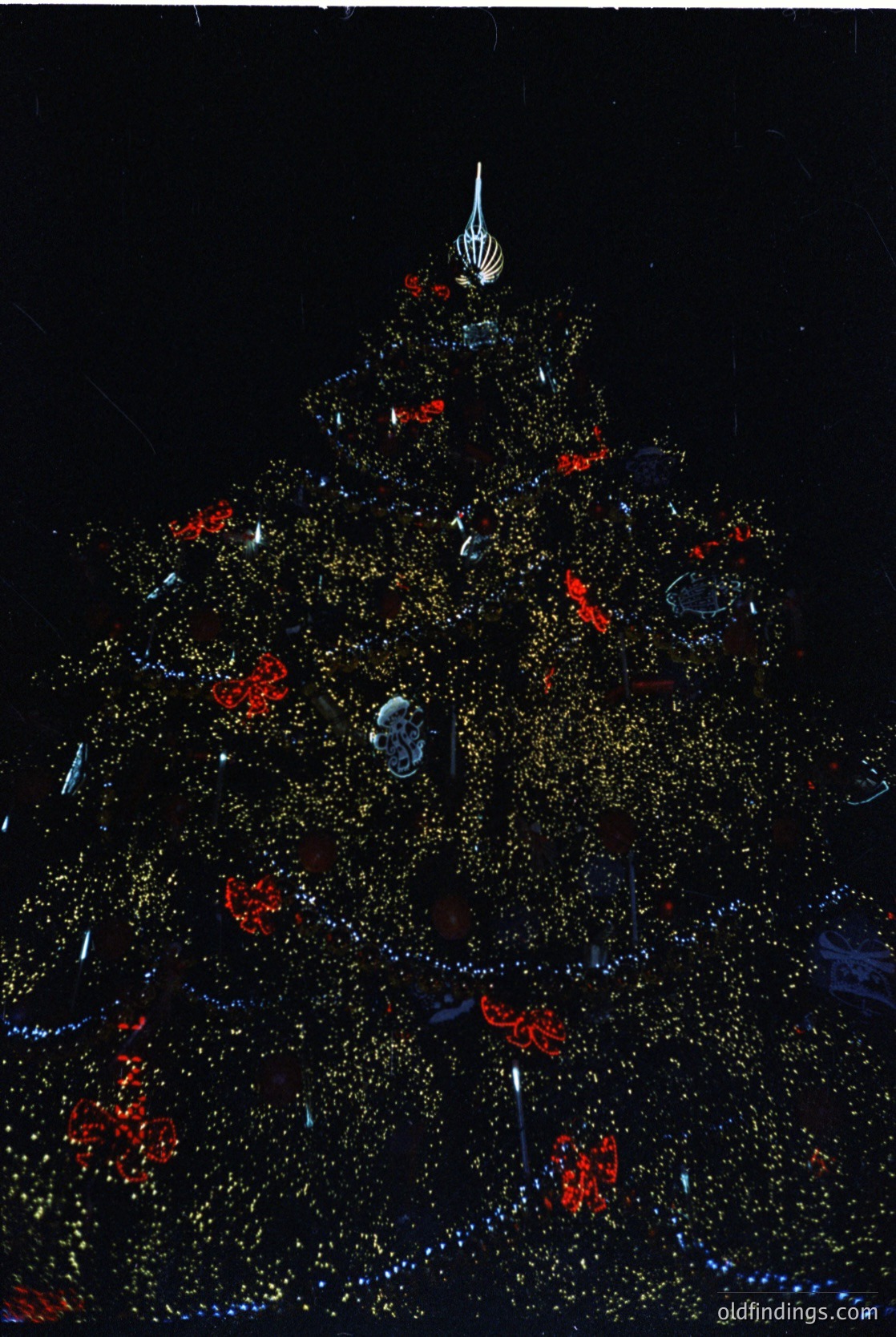 Luminous Christmas tree display with geometric, pyramid-shaped structure adorned with golden and red LED lights, forming intricate floral and star patterns. Likely a modern holiday installation, possibly for festive events or urban decorations.