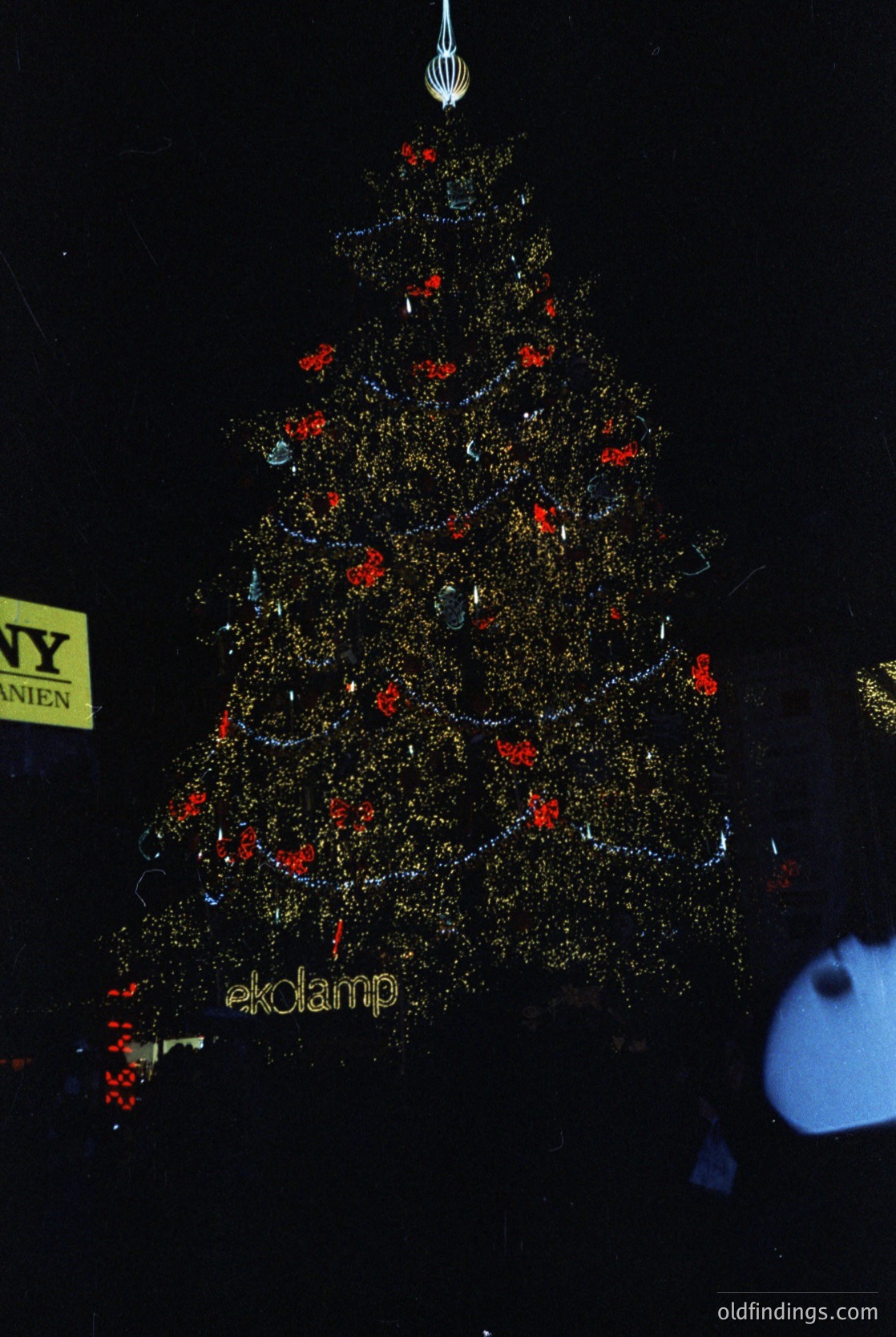 Elaborate metallic Christmas tree display by **ekolamp**, featuring gold-tinted reflective branches and red ornaments. Partial signage suggests NYC location, likely a festive urban holiday installation.