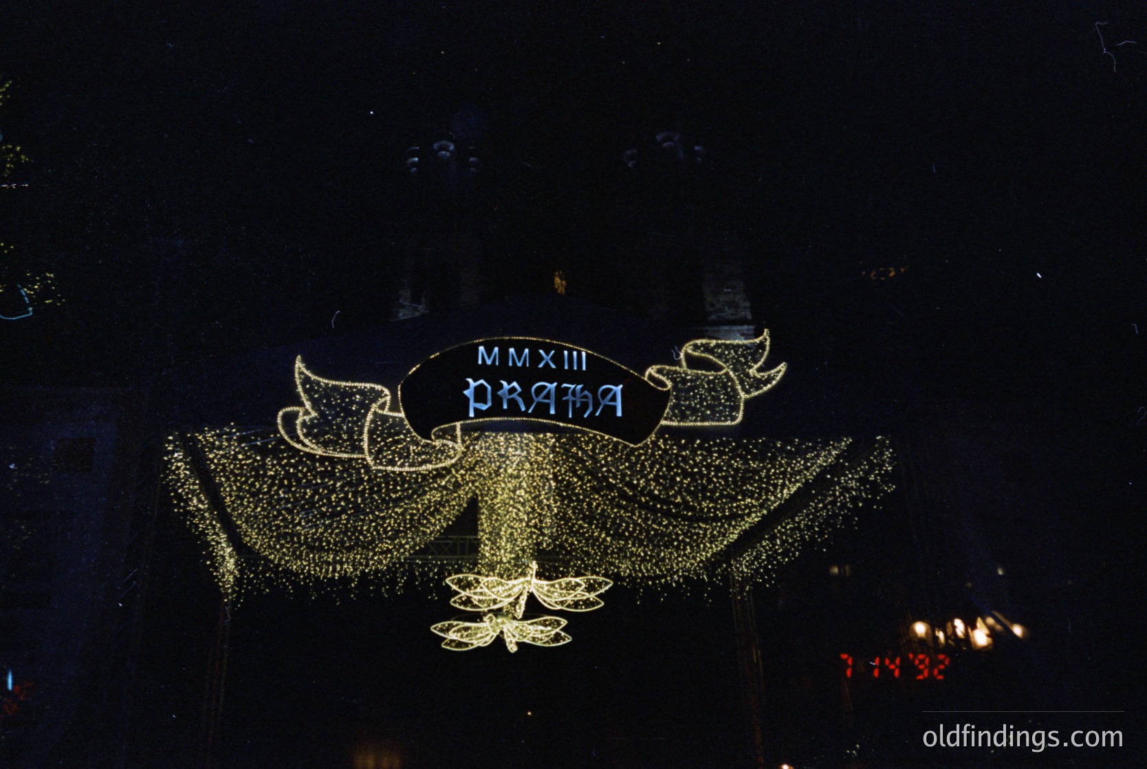 Elaborate illuminated sign featuring Roman numerals "MMXIII" (2013) and "PRAHA" on a decorative, star-studded backdrop. Likely part of a Prague holiday or anniversary celebration.