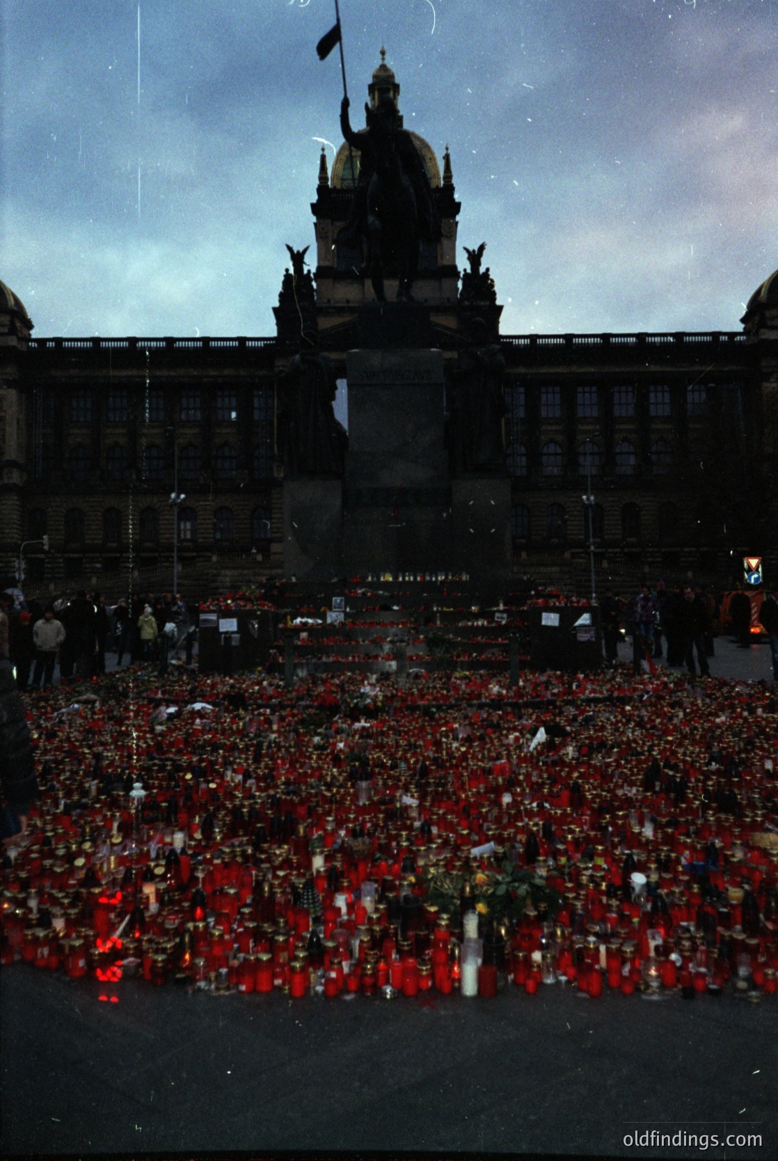 Historic memorial in Prague’s Wenceslas Square featuring a dense arrangement of red candles and floral tributes. The backdrop includes the ornate **National Museum** with its dome and statues. Likely post-2015, following tragic events. Evokes solemnity and remembrance.