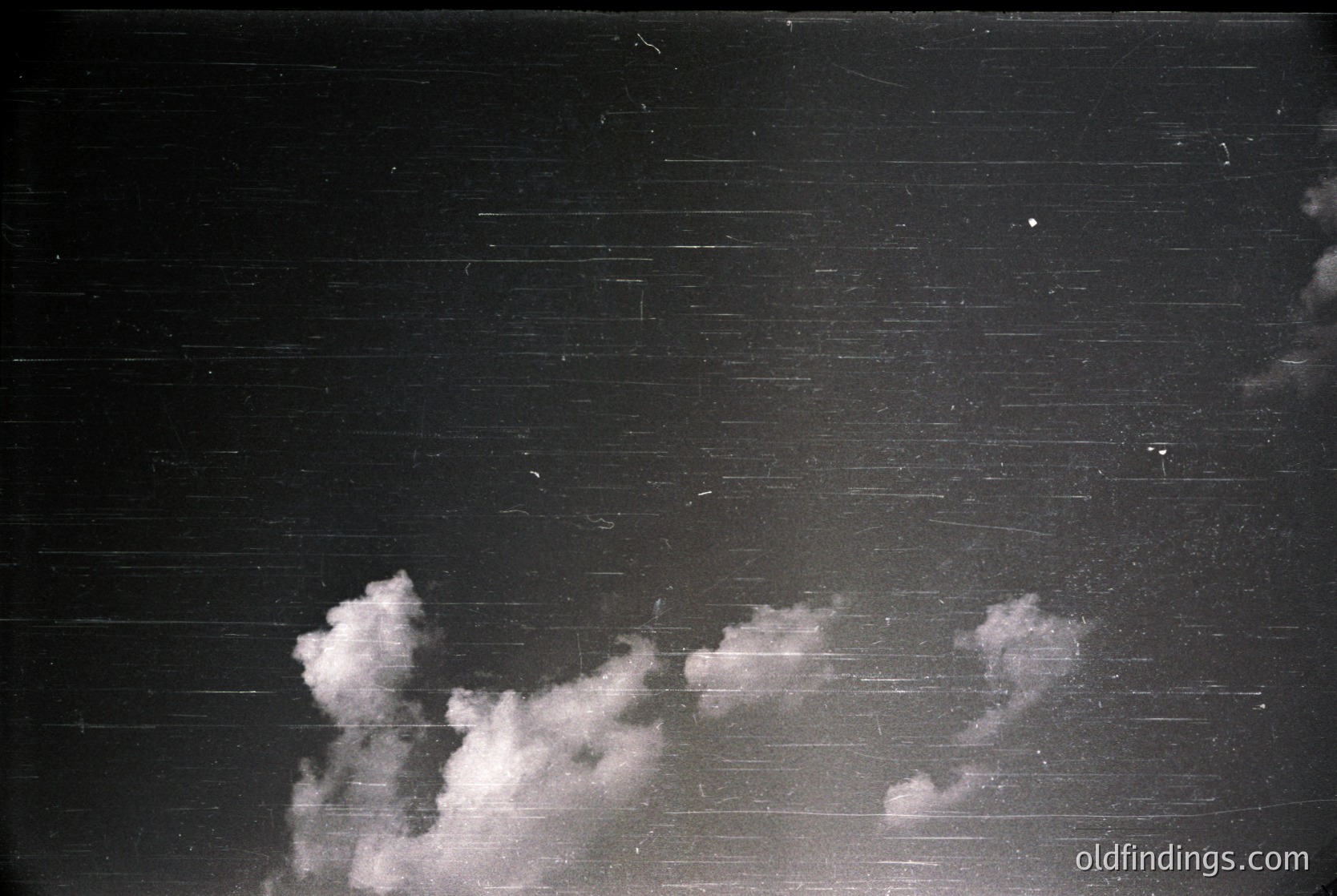 Vintage black-and-white shot of dramatic clouds against a dark, textured wall—likely brick or concrete. The contrast highlights atmospheric textures, evoking industrial or urban architecture. Potential mid-20th century setting ().