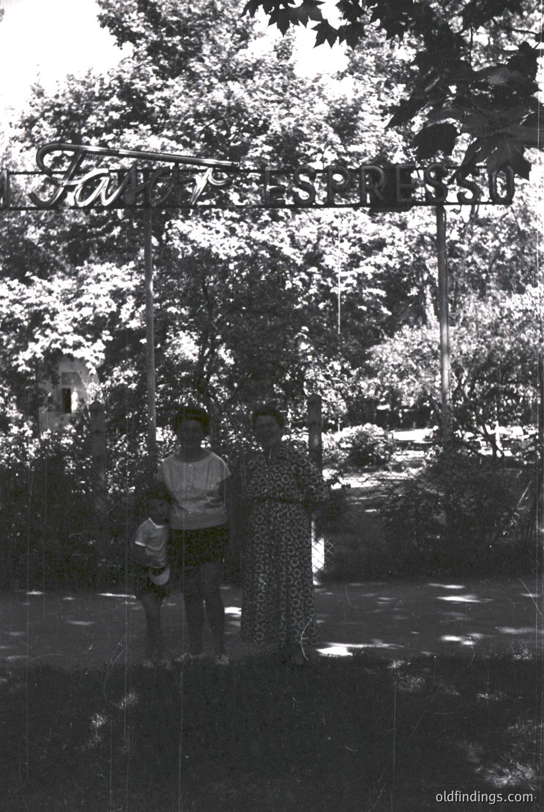 Reflection of a child in a mirrored glass door, framed by lush greenery and a sign reading "Kinderpark" in Cyrillic. Likely Eastern European, mid-20th century.