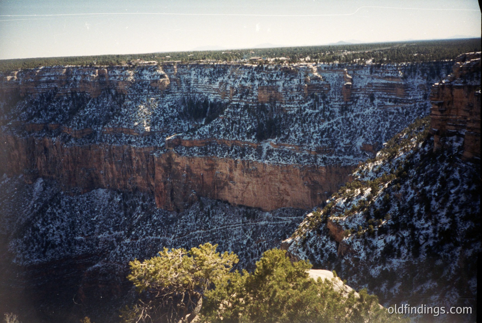 Aerial view of layered red rock canyons with sparse vegetation, likely Grand Canyon, Arizona. Snow patches highlight elevation contrast. Early 20th-century color photography captures dramatic geological formations and vast desert landscape.