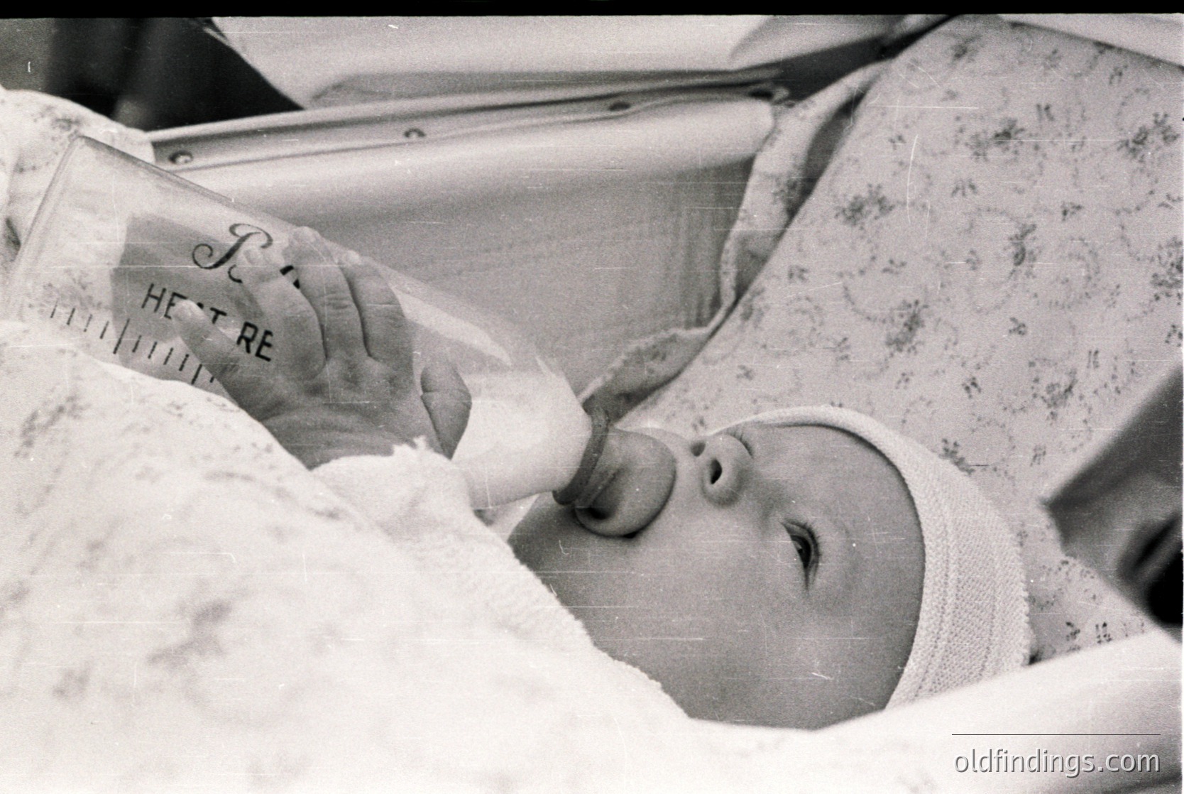 Mid-20th century infant in hospital incubator with "HEAT" label on warming unit. Medical setting with patterned hospital blanket. Likely 1950s–1960s neonatal care.