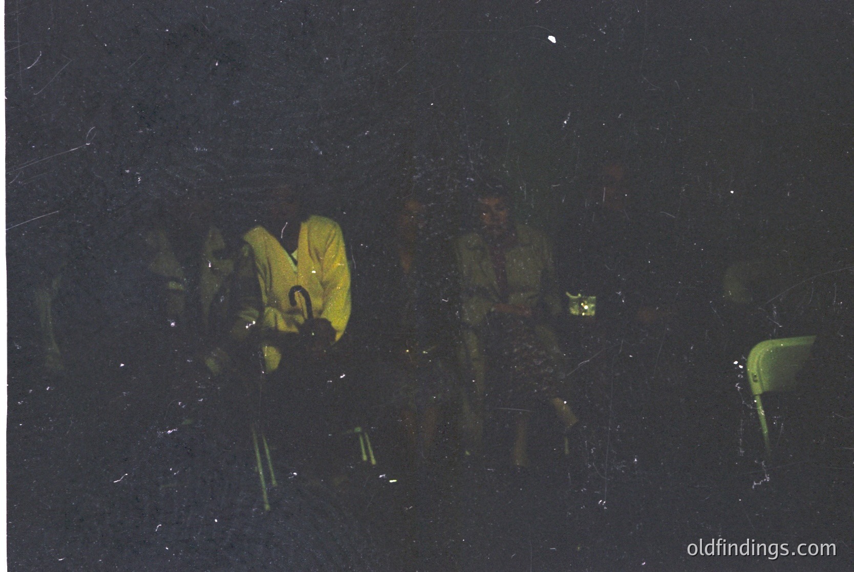 Three figures in camouflage gear and yellow jackets stand on a snowy slope under night sky, illuminated by a single light source. Likely military or winter training exercise, 1970s–1990s era.