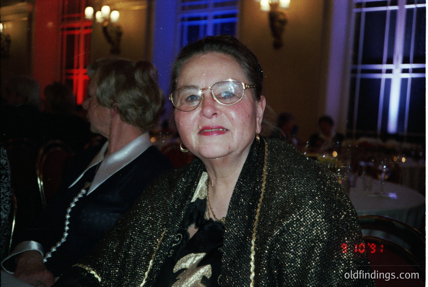 Elegant woman in a shimmering gold sequin coat, framed by dim indoor lighting with a clock displaying 20:31. Formal evening attire suggests a 1990s–2000s gala or upscale event.