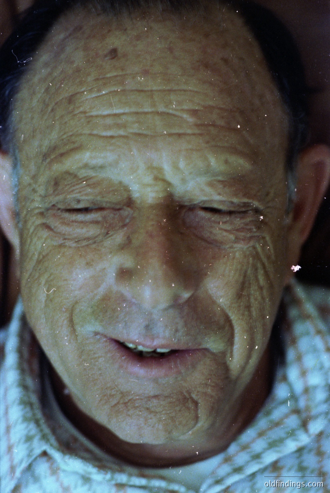 Close-up portrait of an elderly man with a relaxed, serene expression. Skin shows natural aging lines and a faint smile. Light droplets suggest recent water exposure, possibly from a shower or pool. Mid-century styling hints at a or aesthetic.