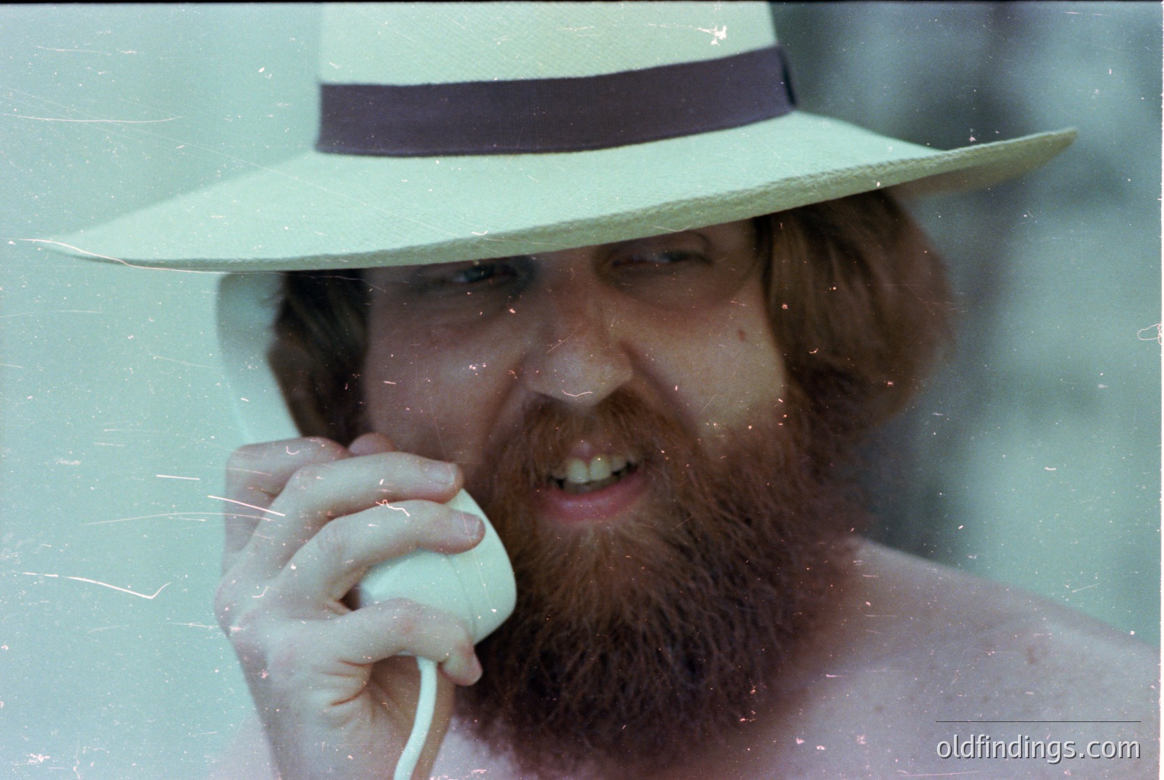 Vintage portrait of a bearded man in a wide-brimmed fedora, holding a retro rotary phone. Lighting suggests indoor studio setting, likely mid-20th century (1950s–1970s). Classic styling evokes nostalgia for analog communication and mid-century fashion.