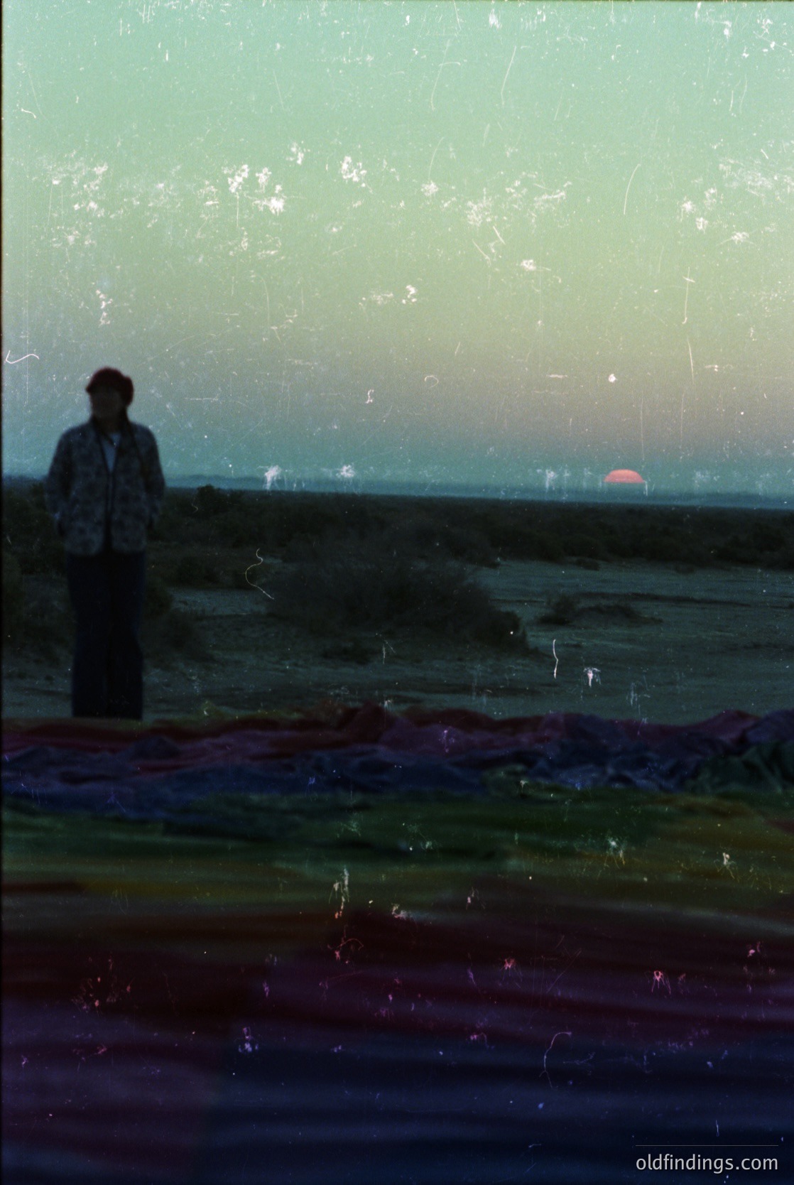 Vintage photograph of a lone figure silhouetted against a sunset, standing on a wet, reflective surface near water. The scene suggests a seaside or lakeside setting with muted tones and a faded, textured overlay. Likely mid-20th century due to style and grain.