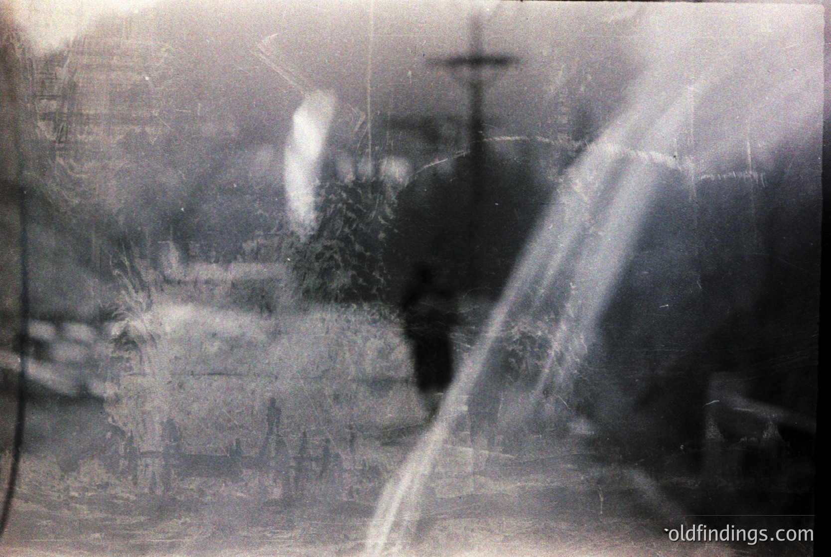 Vintage monochrome photo with heavy vignette and motion blur, likely from a handheld camera. Blurred figures suggest urban street scene with indistinct architecture and a visible cross, hinting at a European cityscape. Artistic grain and soft focus evoke 1960s–1980s film photography.