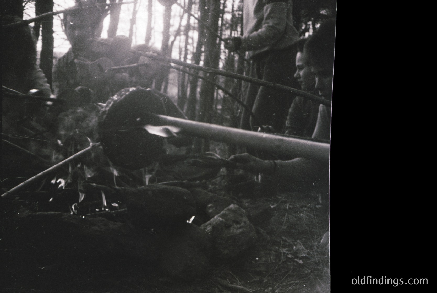 Black-and-white wartime scene: soldiers in dense forest, one soldier lying prone with rifle raised, others crouched or standing behind him. Likely Eastern Front, 1940s.