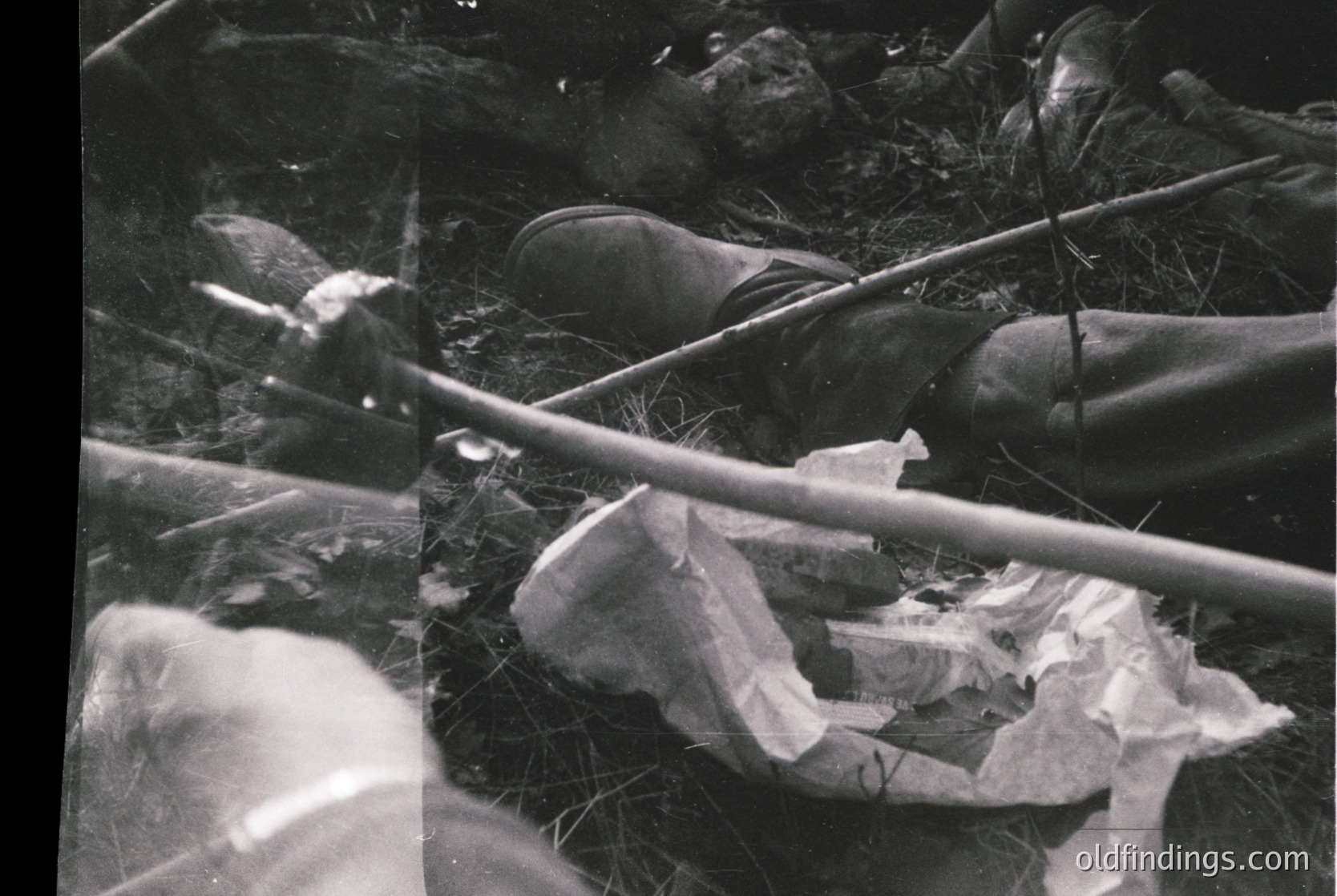 Black-and-white close-up of discarded items in a grassy area: crumpled paper, a broken bottle, and a twisted metal rod. Evidence of littering in an outdoor setting, likely mid-20th century due to film grain.