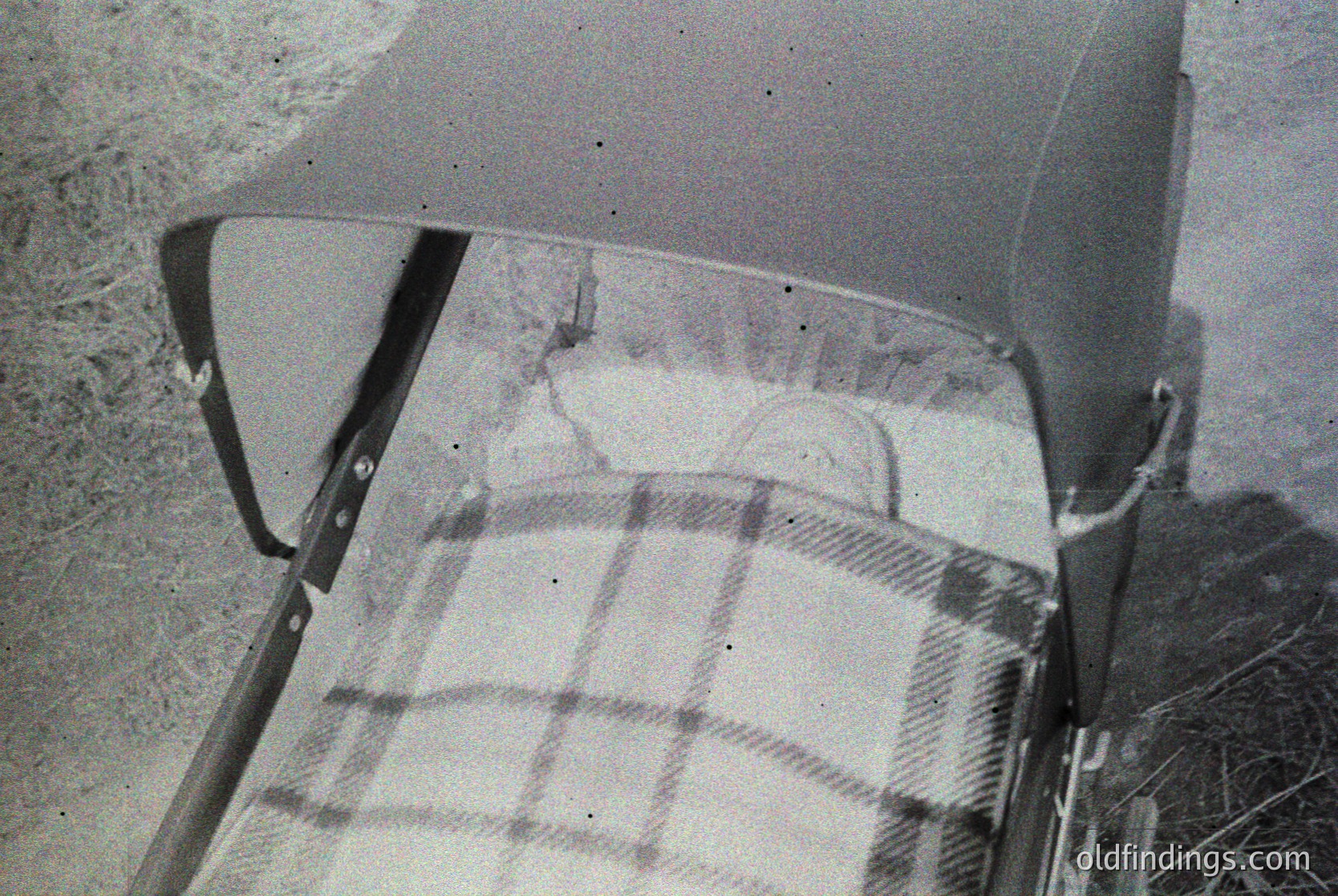 Close-up of a vintage car’s rear passenger seat with a plaid blanket draped over it, suggesting mid-20th century design. Visible stitching and worn fabric detail indicate practical, utilitarian use. --- *Note: The image lacks clear geographical or time-specific indicators beyond mid-20th-century automotive design.*