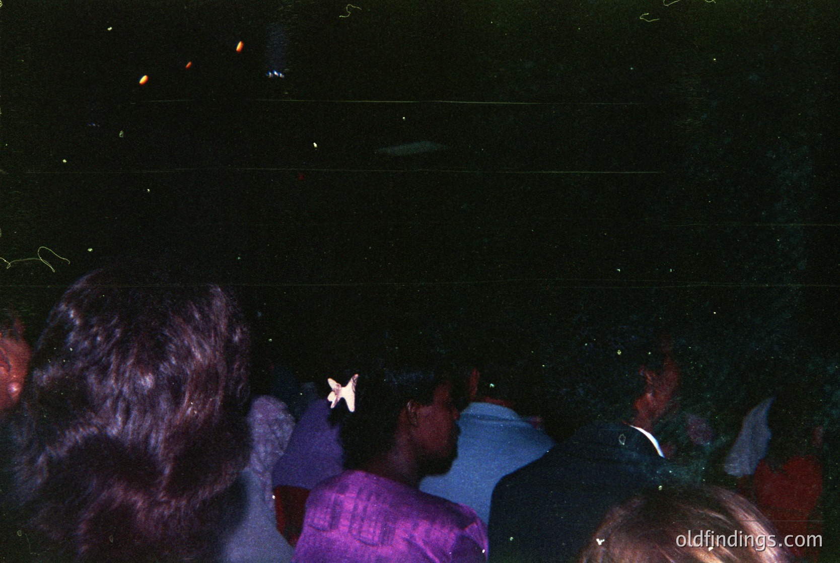 Vintage nightclub scene with blurred crowd under disco lighting. Central figure wears a purple shirt and holds a white paper airplane. Motion blur suggests rapid movement and energetic atmosphere. Likely 1970s–1980s disco era.