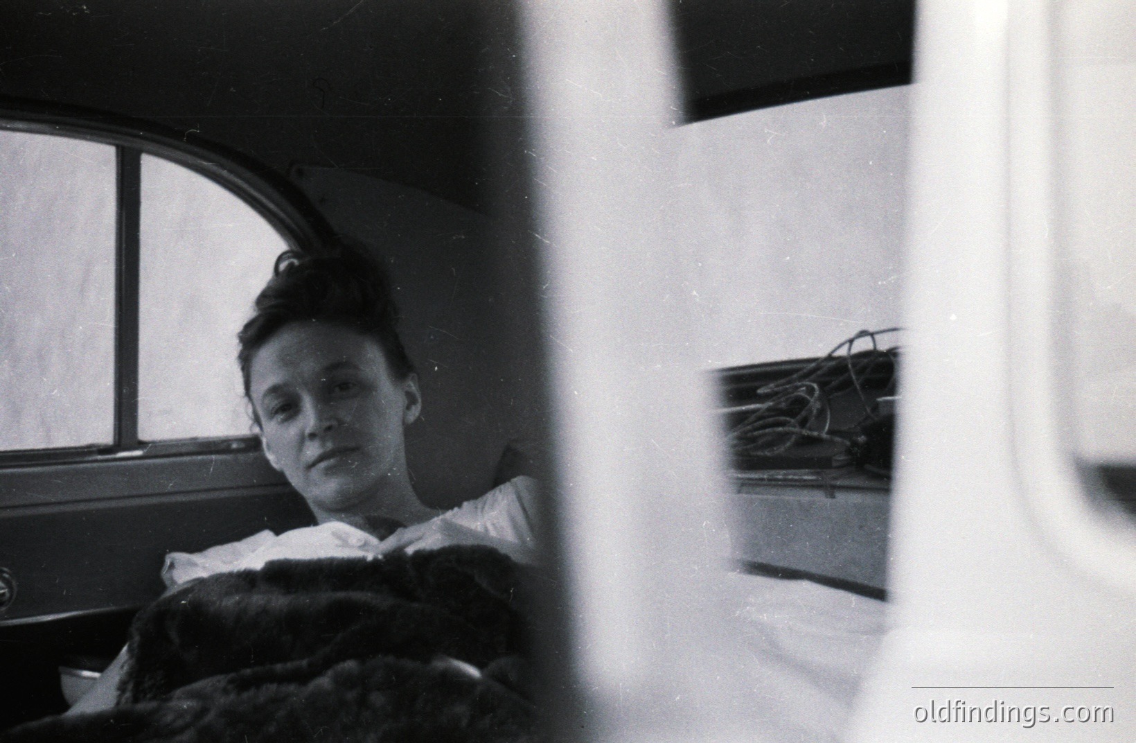 A woman reclines on a bed covered in fur, seen through a window arch. Appears to be in a historic or period setting. Strong use of natural light. Film grain adds texture; potentially 1960s/70s era. Interior shot; quiet, contemplative mood. Potential stock photo reference for vintage aesthetics.