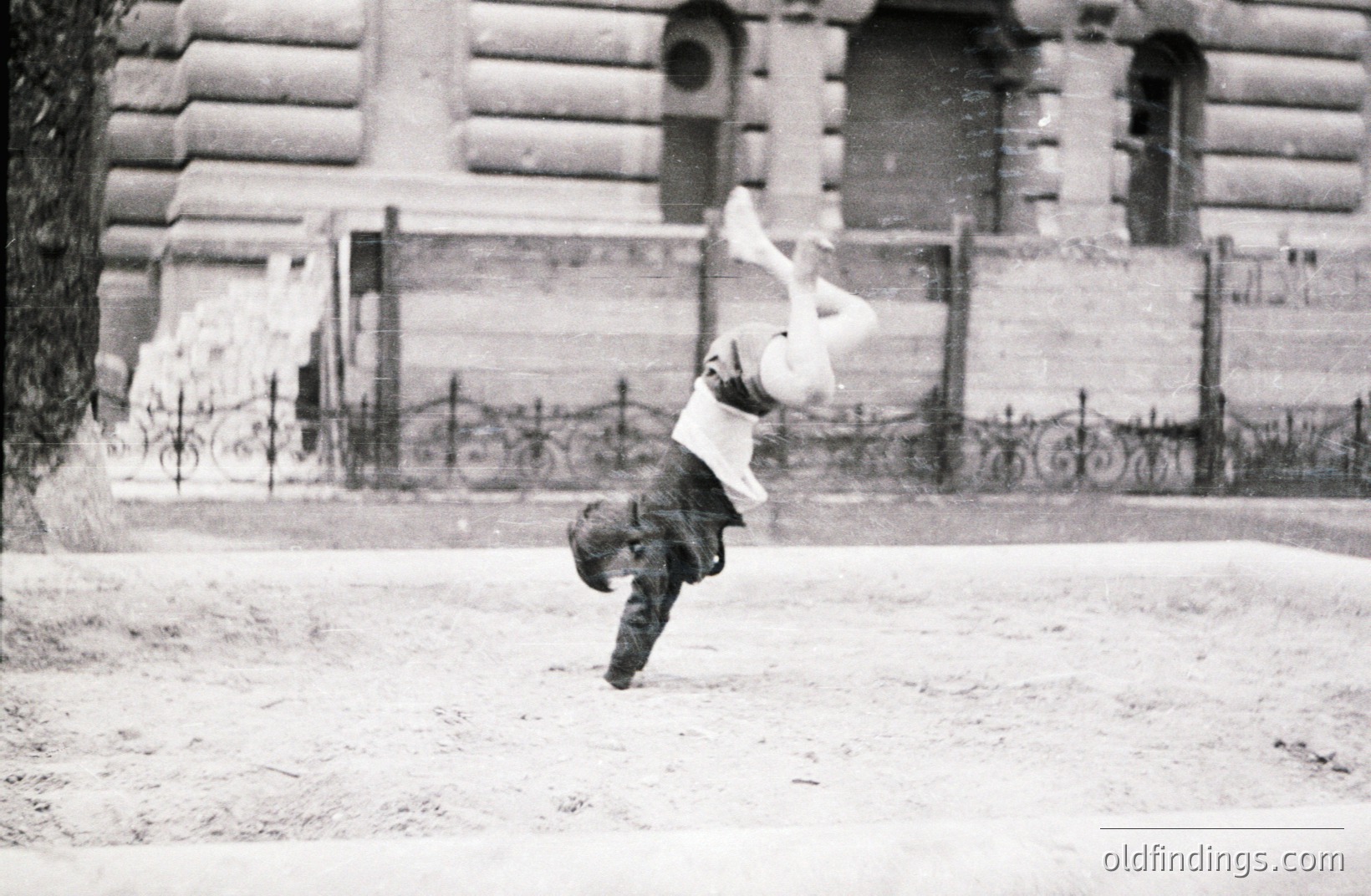 A man mid-fall, captured in a dynamic, candid moment. He's clad in a suit and hat, legs flailing upwards. Architectural background suggests a formal building, possibly government or institutional. Likely a 1920s or 1930s street scene, documenting an everyday mishap. A valuable glimpse into early 20th-century urban life.