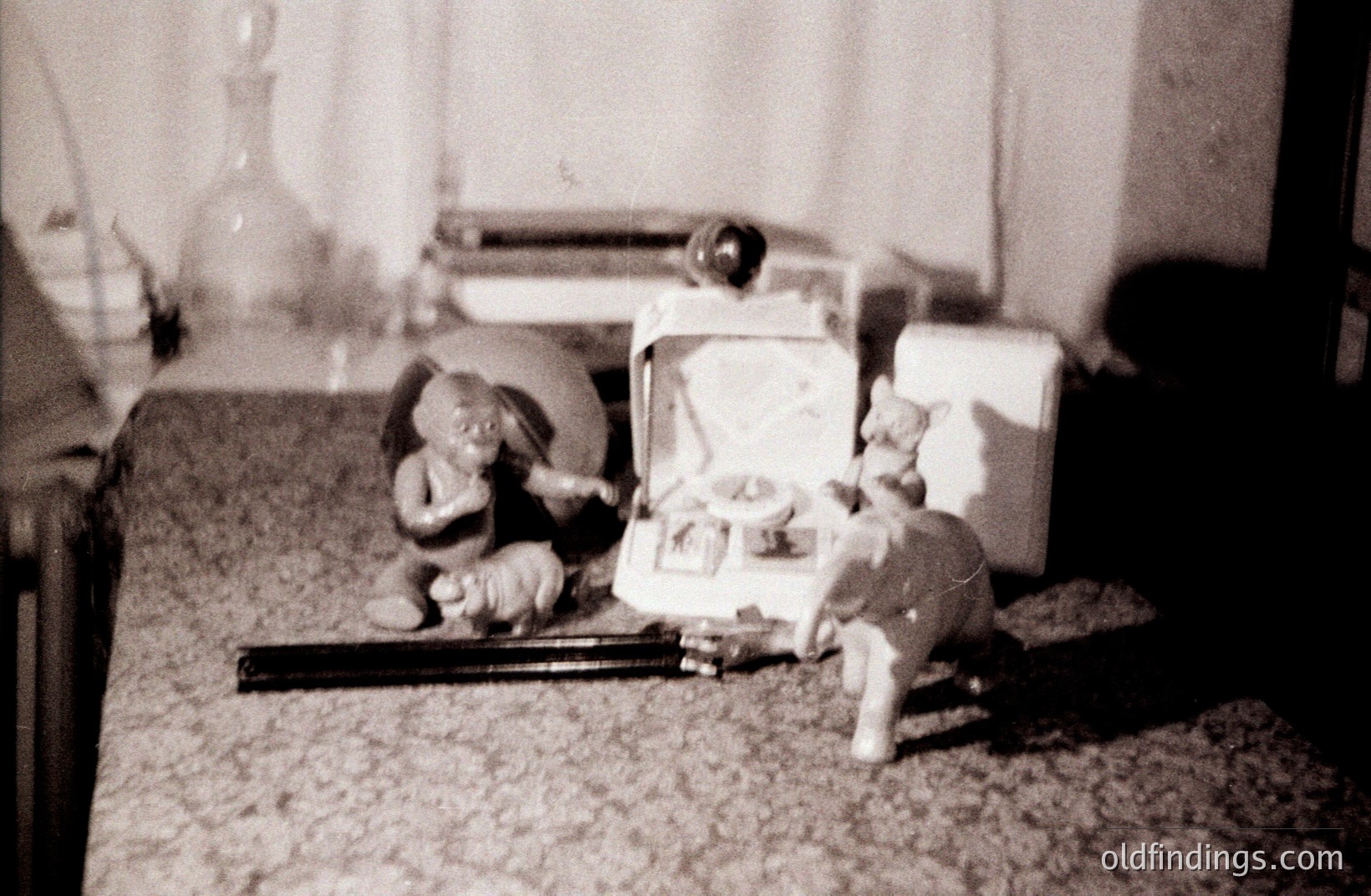 A whimsical scene featuring ceramic figurines: an elephant playing a miniature violin and a cat perched near a vintage portable record player. The texture suggests a textured floor covering. Likely a domestic interior, possibly a child’s playroom. Hints at a mid-century aesthetic.