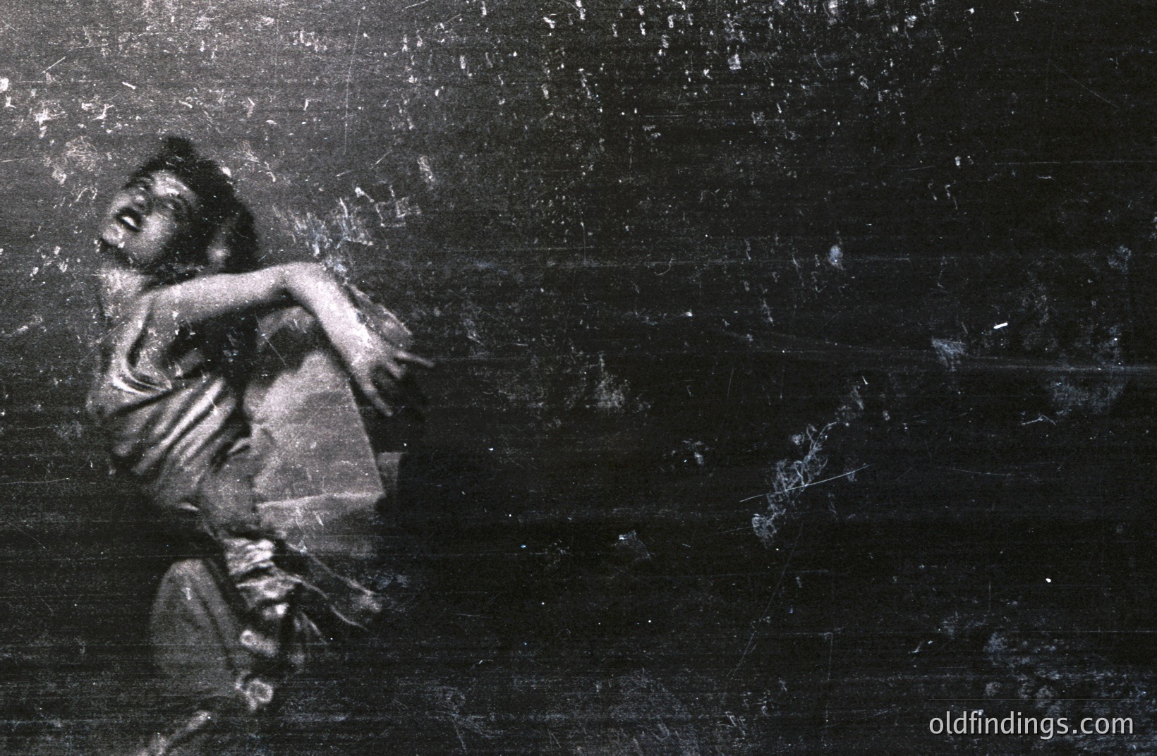 A dancer in mid-motion, captured in a black and white photograph. The subject's arm is extended, creating a dynamic, swirling pose. Visible wear and scratches on the image suggest age and handling. Likely a performance still or rehearsal shot.