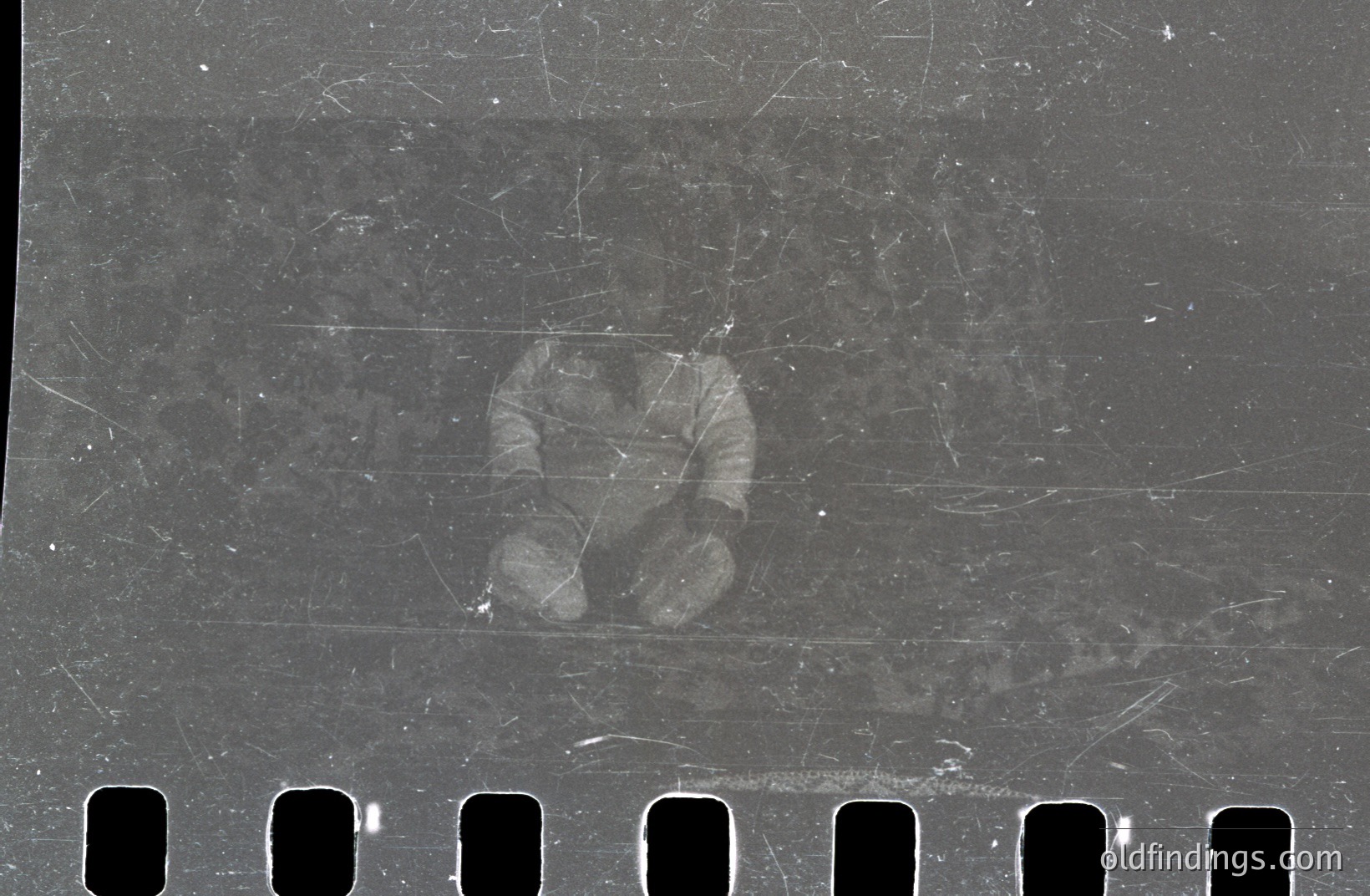 A grainy, partial image of a person's hands in a dark coat, captured on aged 35mm film stock. Visible sprocket holes indicate the film's original format. Image quality is degraded with scratches and dust. Likely a snapshot, its historical value lies in documentation of photographic processes & materials.