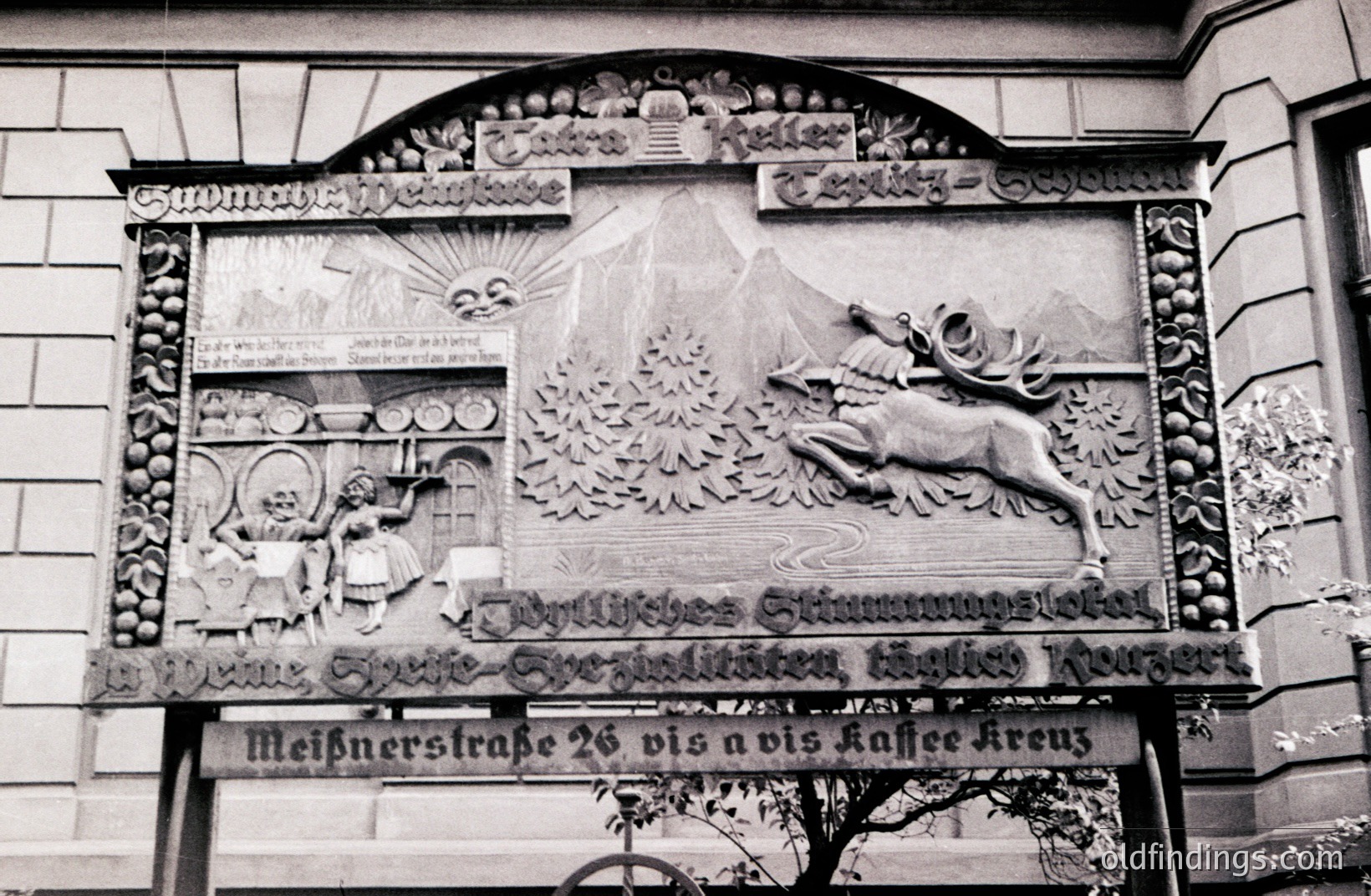 Elaborate stone relief advertisement displays a stylized alpine landscape with a leaping stag and a figure carrying beer barrels. Text identifies it as a beer hall, with address "Meißnerstraße 26." Likely German, late 19th/early 20th century. Displays cultural significance.