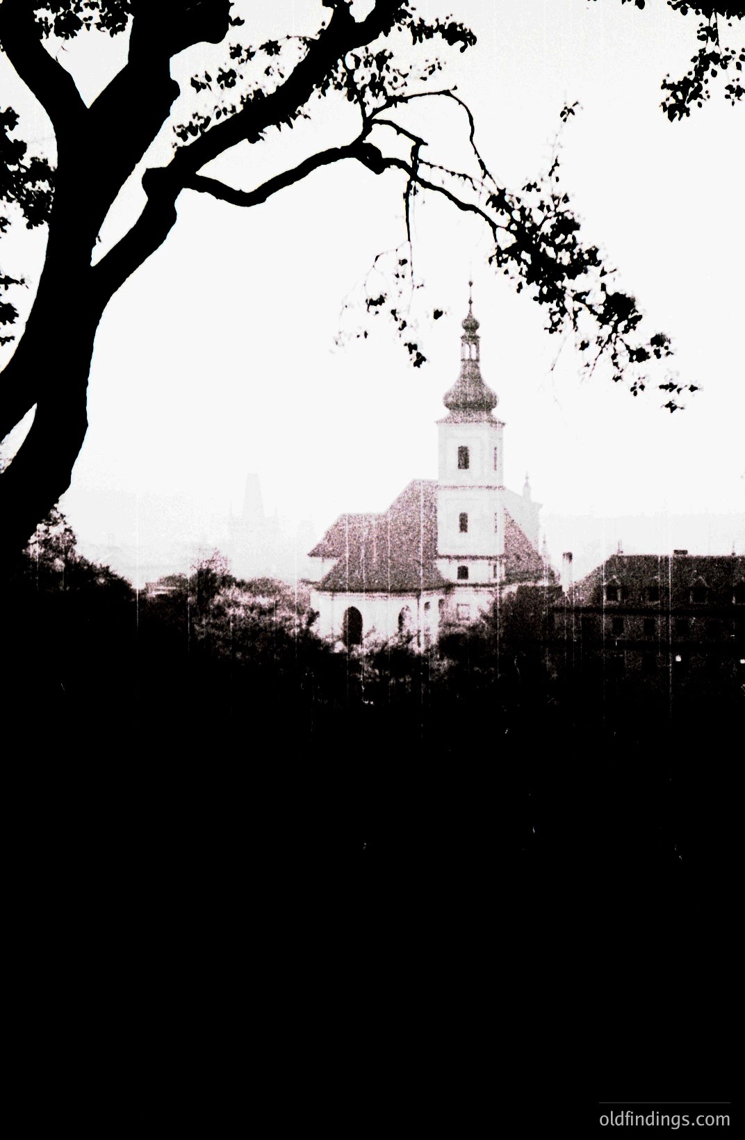 A framed view of a church with a central spire & tiled roof, set within a small village. The image's muted tones & visible grain suggest a vintage aesthetic, possibly 1960s or 70s. Likely Eastern European location, maybe rural Romania. A simple architectural style & overcast sky contribute to the scene.