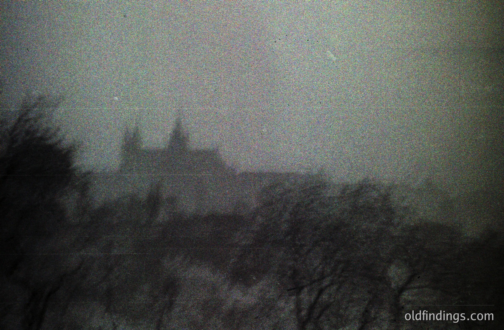 A grayscale image depicts a densely forested area, likely woodland, with a large, ornate building visible through the trees. The architecture appears to be Gothic Revival, featuring multiple towers and pointed arches. High-grain texture indicates a potentially older or low-light photograph. Possible architectural reference for design or historical research.
