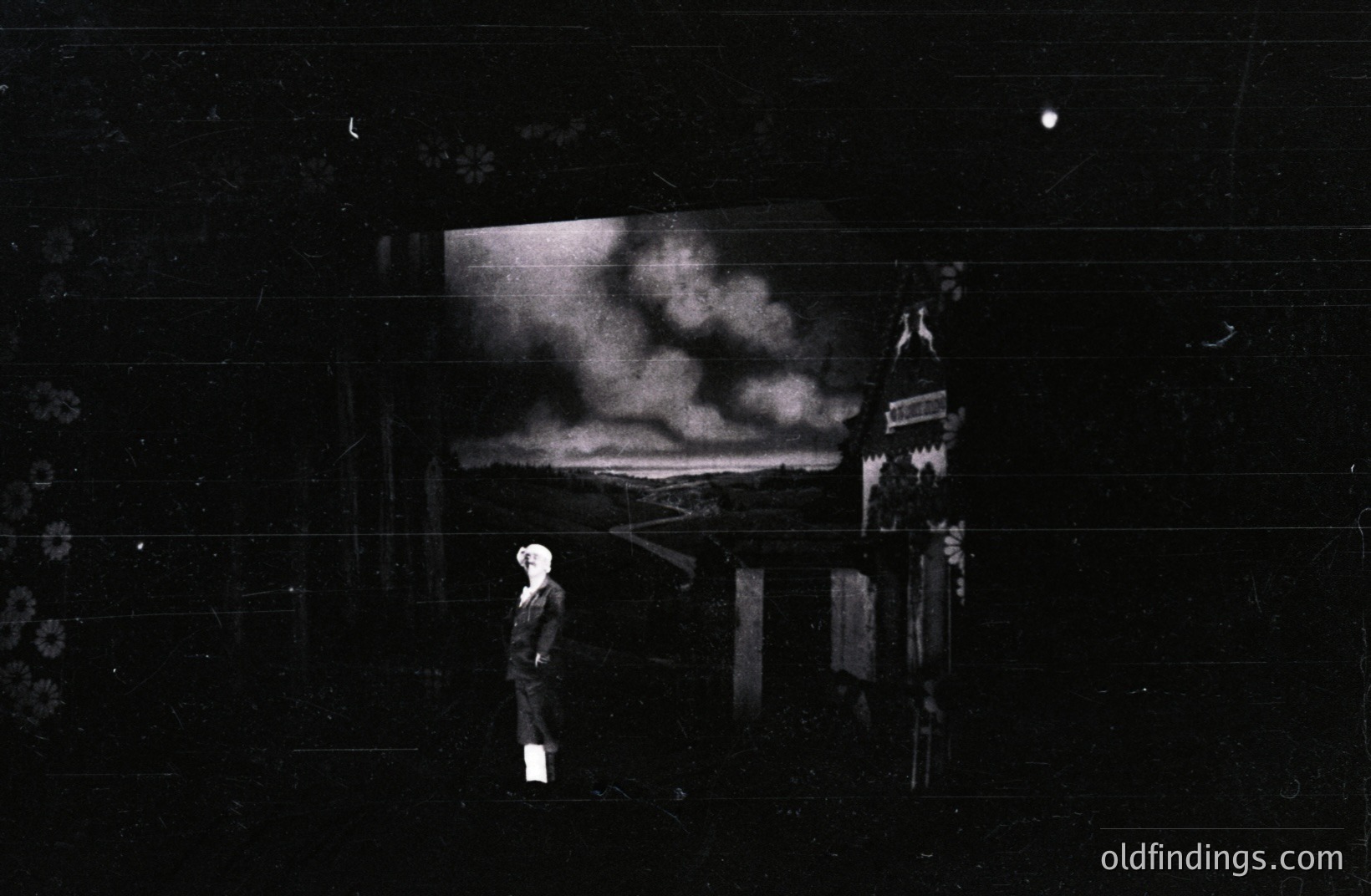 A solitary figure in period attire stands near a damaged building with a panoramic vista behind. Appears to document post-war devastation; likely European, potentially 1940s. Composition emphasizes isolation and architectural ruin. Dusting and film scratches are present.