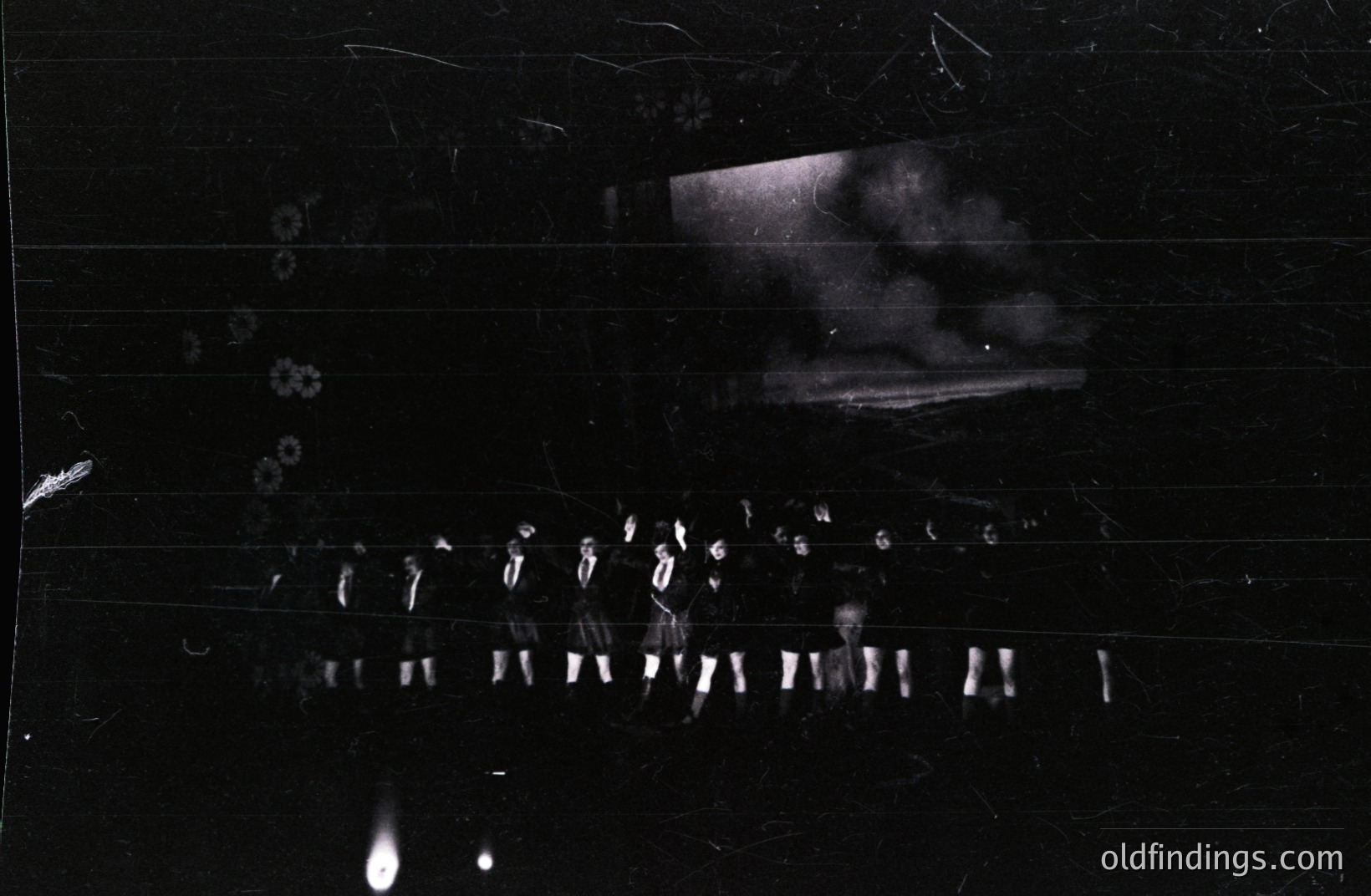 A group of formally-dressed men stand in a row, possibly military or uniformed personnel. The scene appears staged, with a blurred background suggesting an exterior setting. The image exhibits notable film grain and physical imperfections. Likely a mid-20th century institutional or documentary photograph.