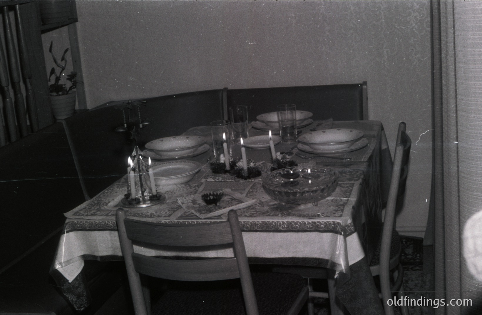 A formal table setting for four is captured in this black and white interior photo. Linen tablecloth, ornate candle holders, and glassware suggest a special occasion. The scene has a vintage aesthetic, likely from the 1960s or 70s. Good for design reference.