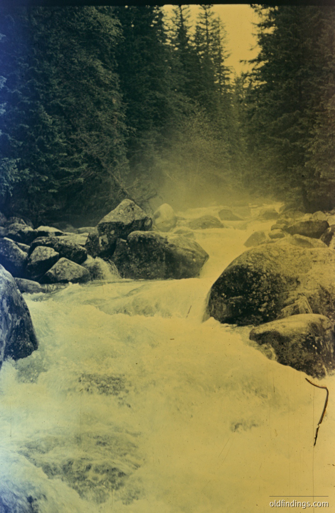 A rushing, rocky river carves through a forested landscape. Visible water movement suggests long exposure. Sepia-toned photograph, potentially from the mid-20th century, capturing a natural, untamed scene. Evidence of photo manipulation/darkening at the edges. Photographic reference material.