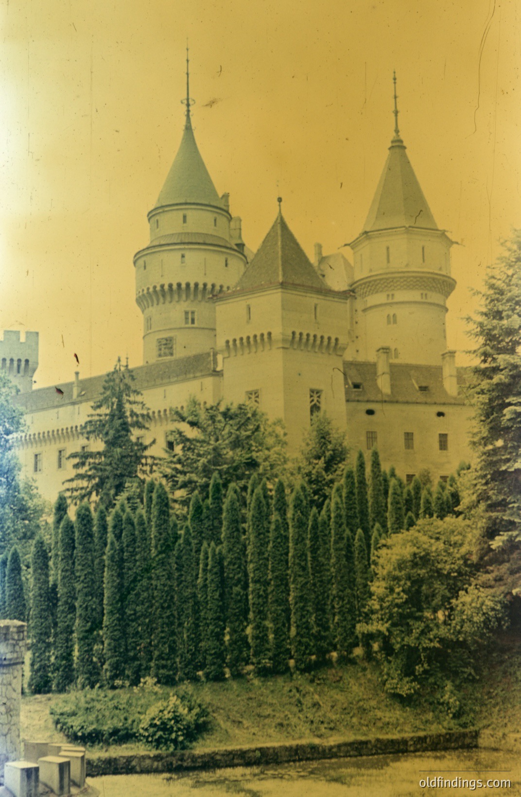 A view of Peleș Castle, Romania, showcasing its distinctive neo-Renaissance architecture and tiered turrets. The building blends into the landscape with carefully manicured topiary hedges in the foreground. Likely dating from the late 19th/early 20th century, captured on vintage photographic film. A valuable reference for architectural studies. șCastle