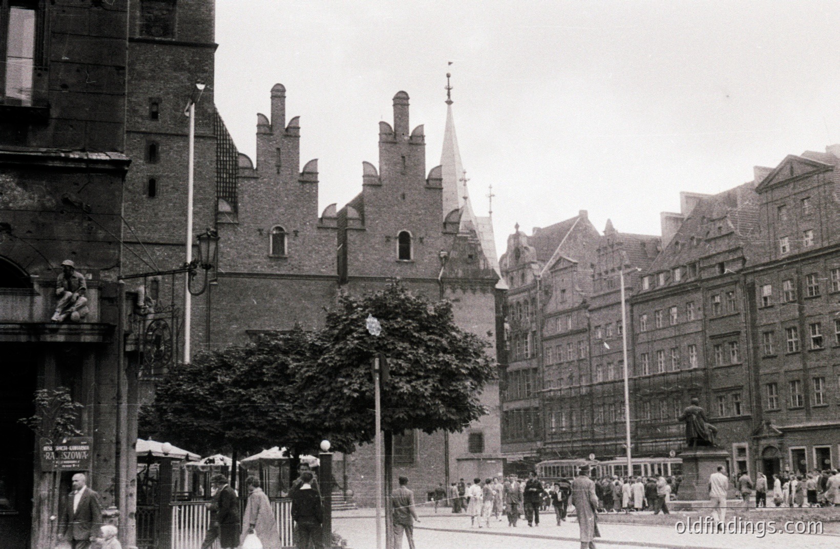 Black and white street scene captures a European city's historic center. Prominent gabled buildings feature elaborate brickwork and decorative spires. Pedestrians and vehicles populate the paved street. Likely mid-20th century, architectural style suggests Northern Europe. Potential commercial value for design references or historical research.