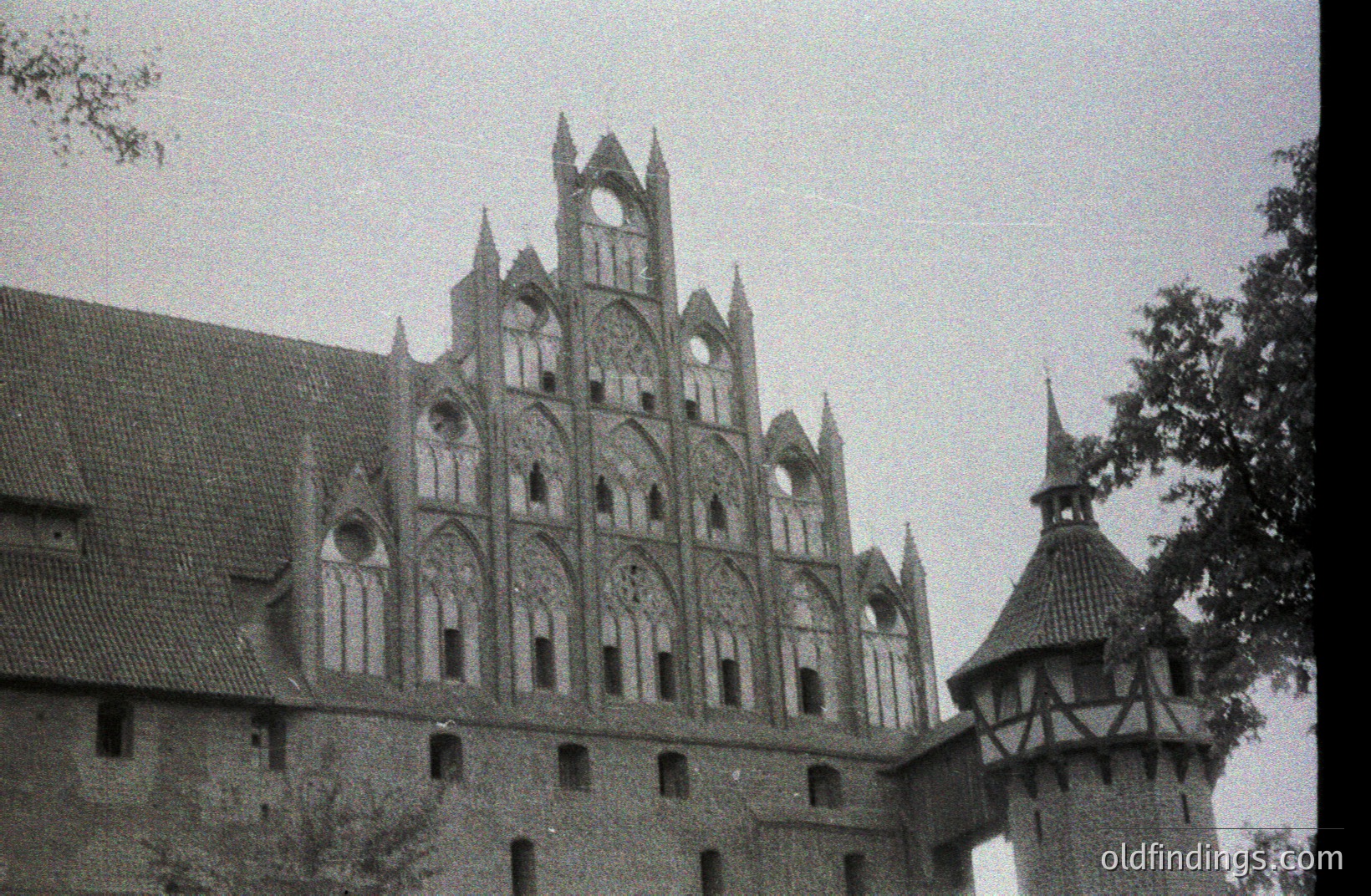 Striking facade of a Gothic brick building, likely a church or castle. Detailed tracery and pointed arches define the upper levels. Timber framing visible on a corner tower. Possibly Northern or Eastern Europe, circa 1930s-1960s. A valuable reference for architectural studies.