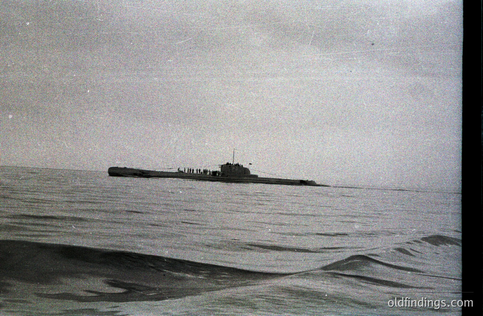 A large submarine cuts through a choppy sea. The vessel's conning tower and deck structures are visible against a heavily overcast sky. Likely a post-WWII era naval exercise or training operation. The grainy texture suggests a mid-20th century black-and-white photograph.